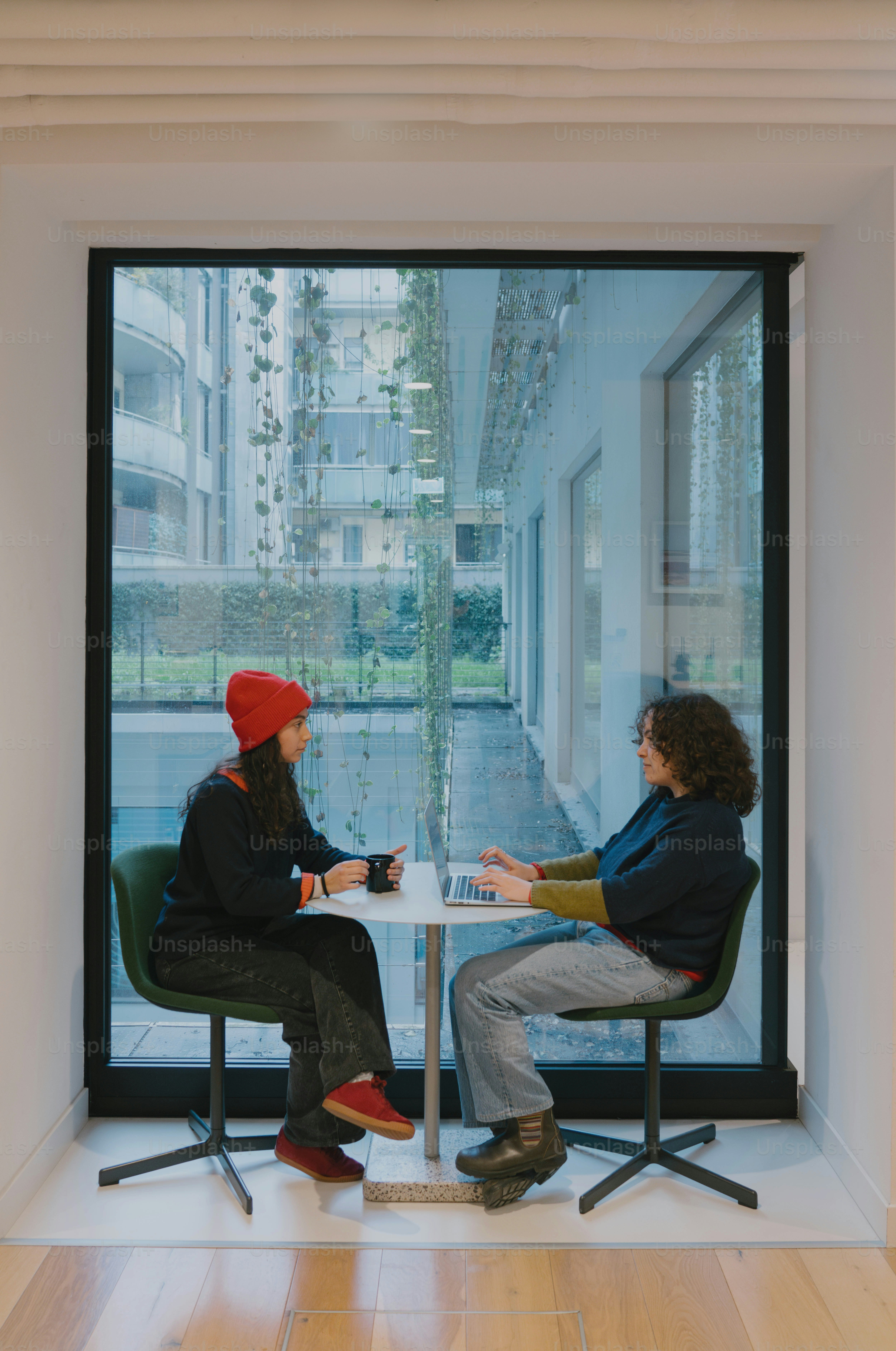 Two people sit at a table in front of a window.