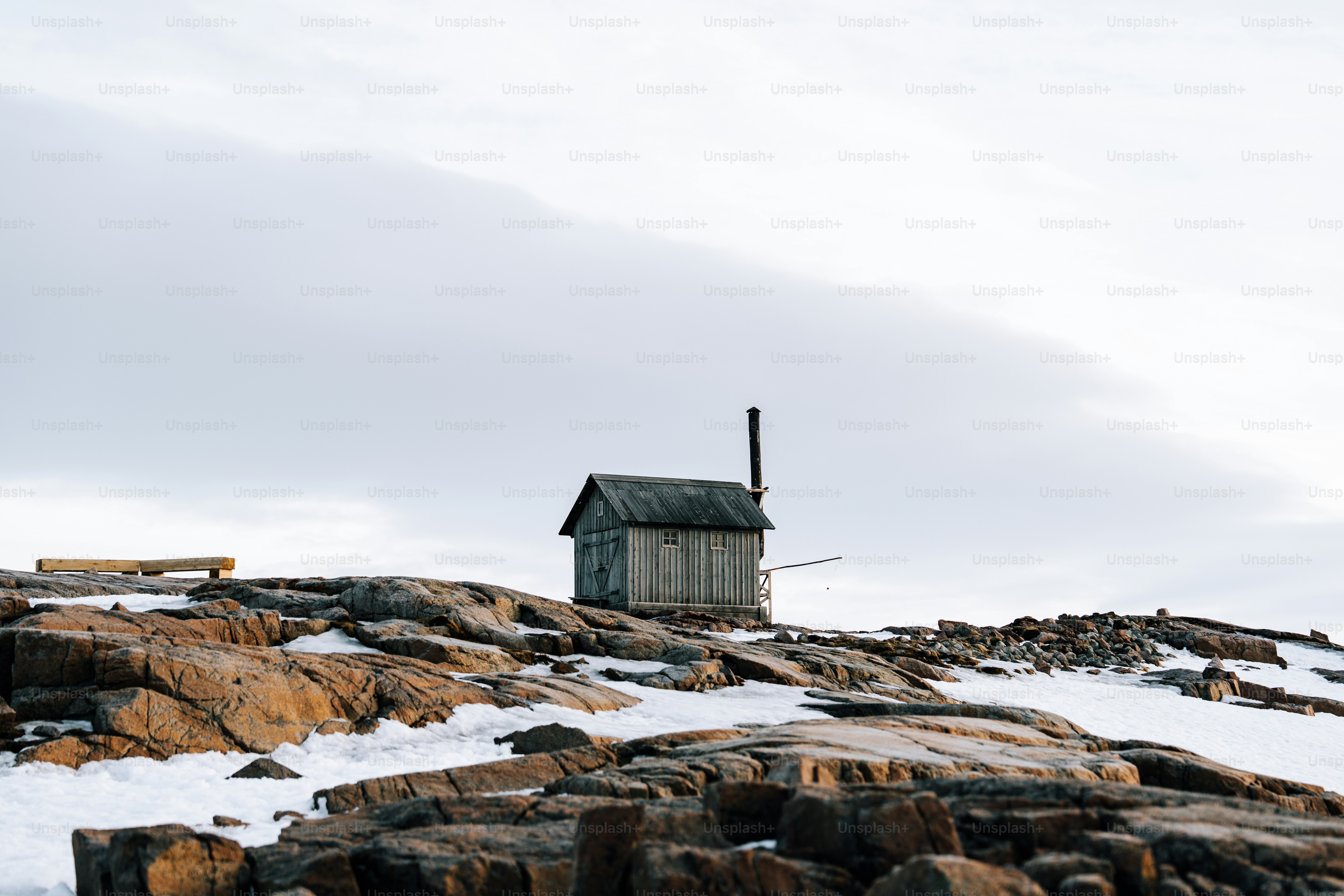 A small shack sits on a snowy, rocky hill.