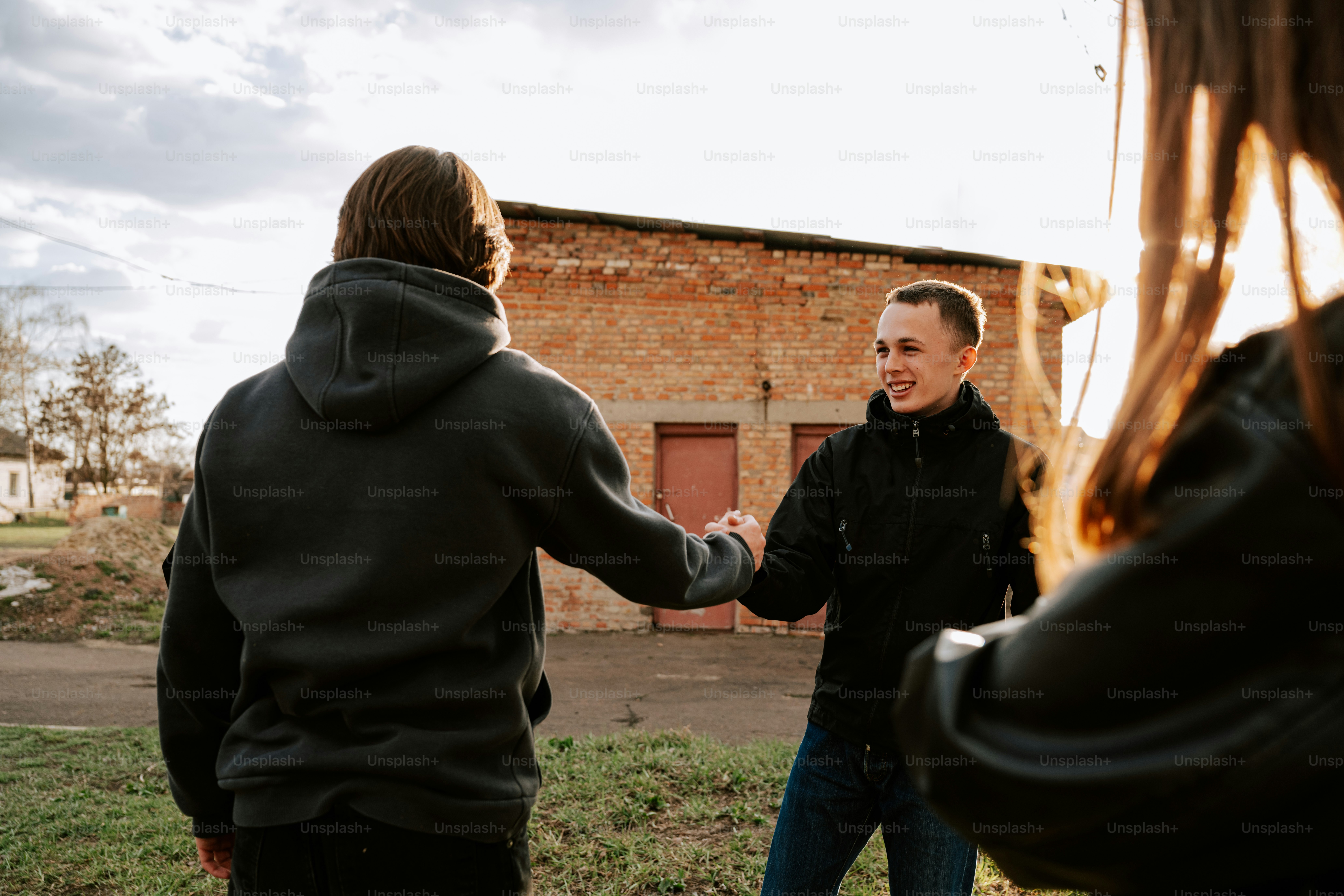 Friends greet each other outdoors, holding hands.