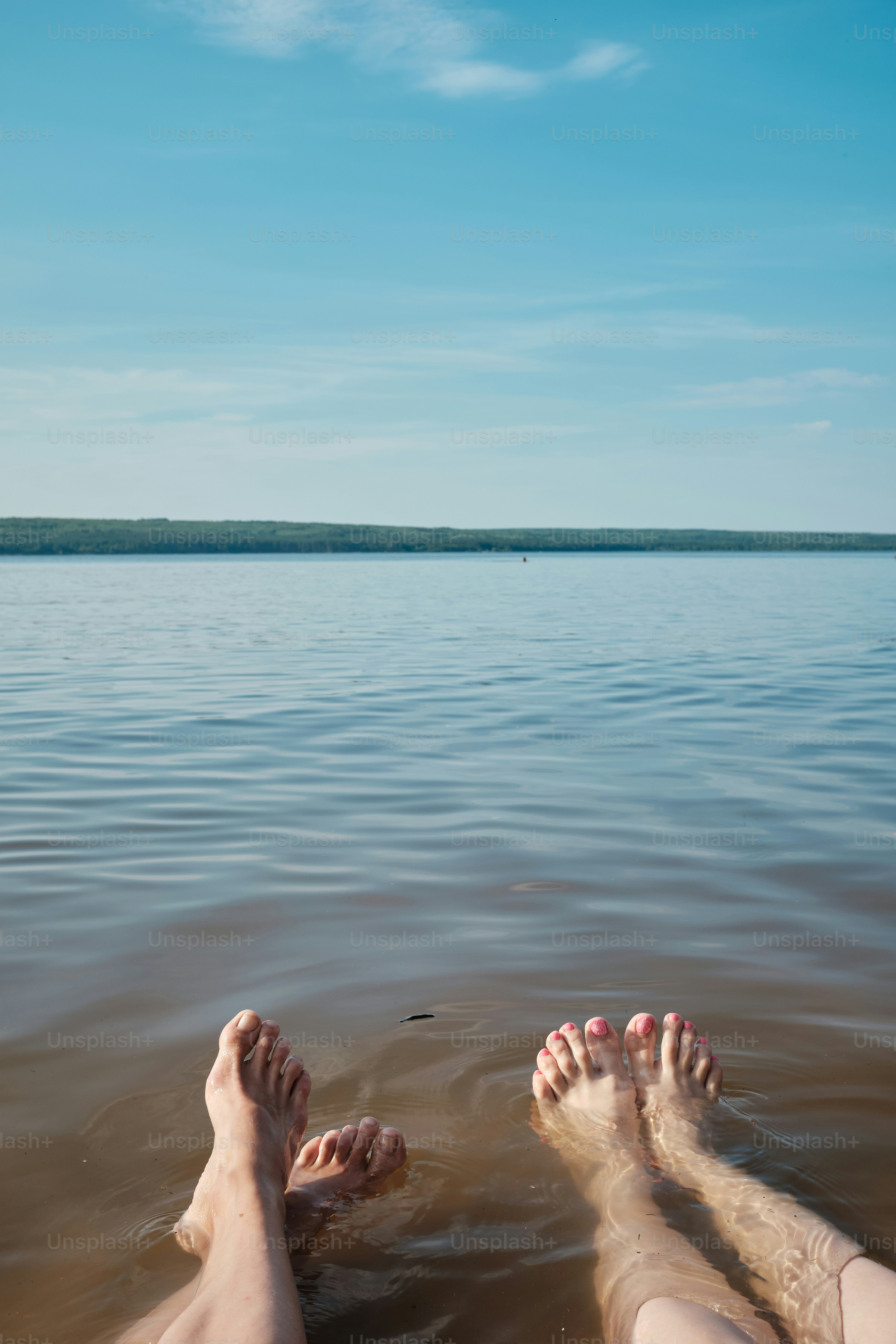 Feet dangle in water under a beautiful blue sky.
