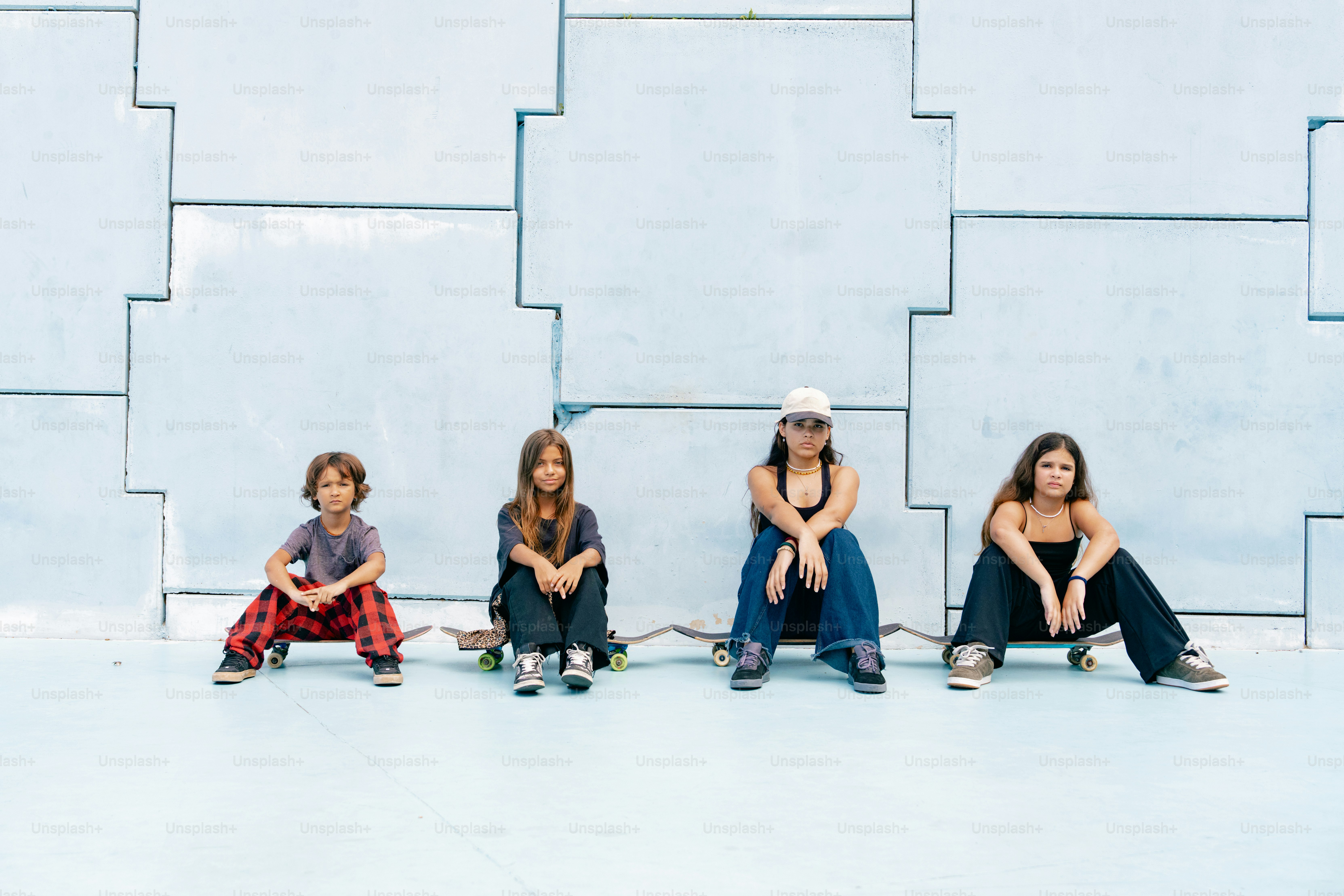 Four kids sit on skateboards against a wall.