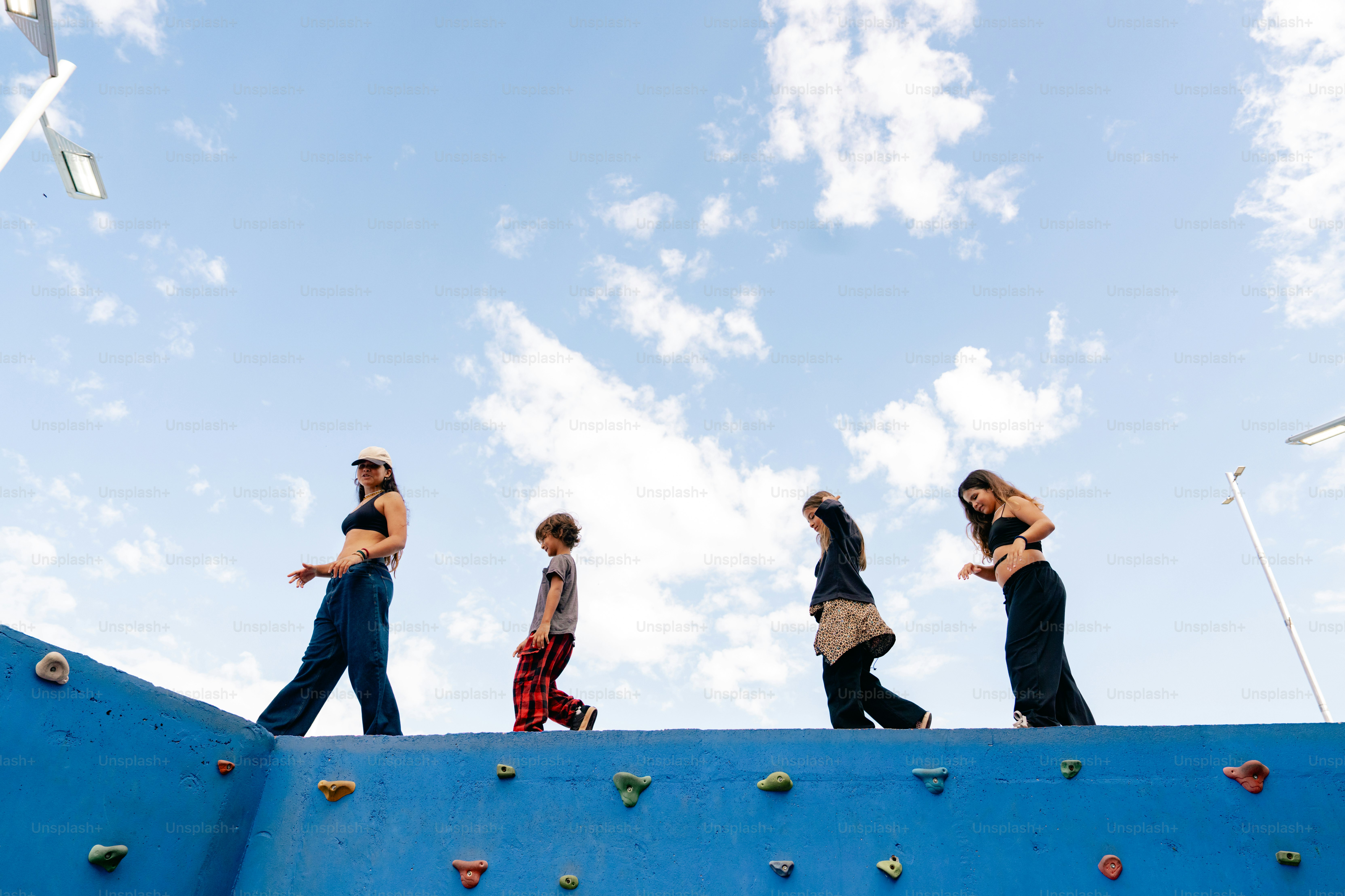 People walk along a blue wall under a cloudy sky.