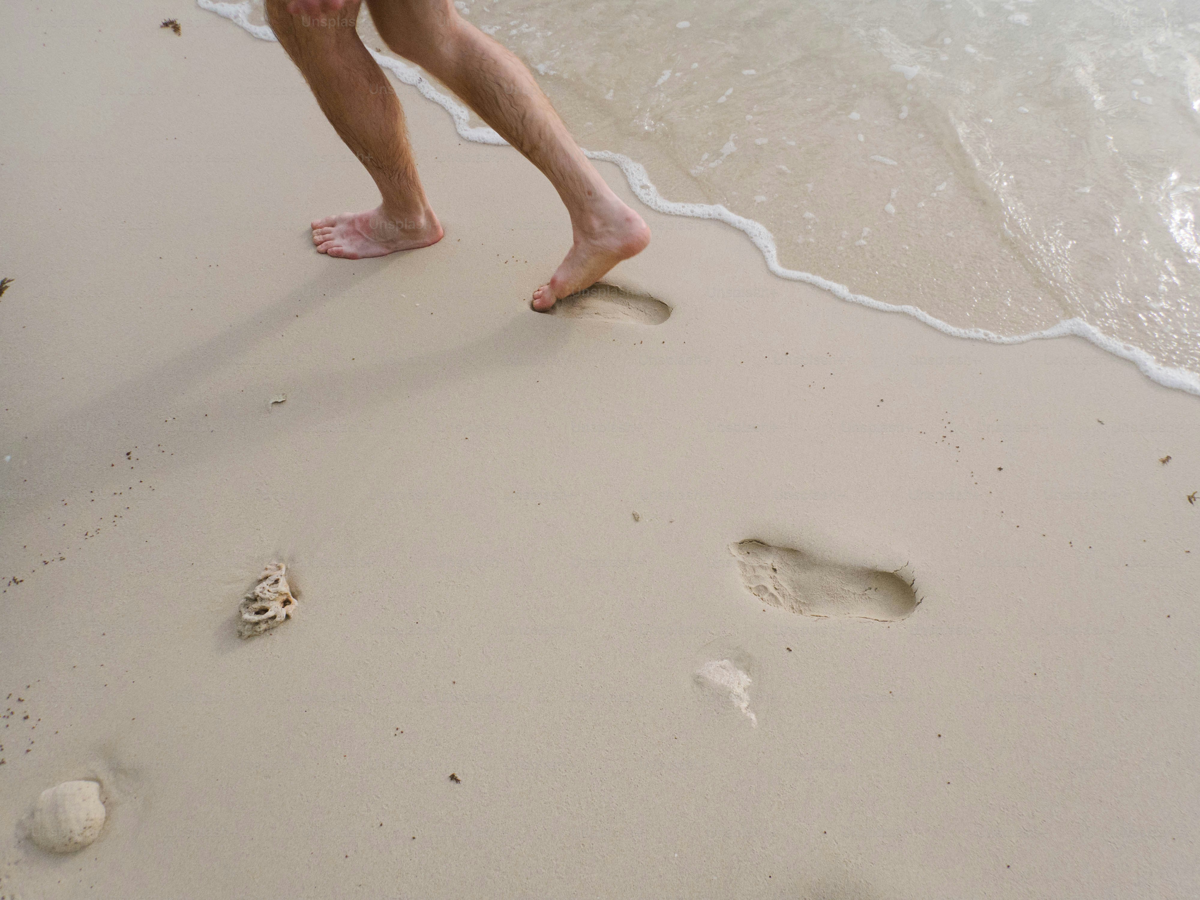 Bare feet walk along a sandy beach.
