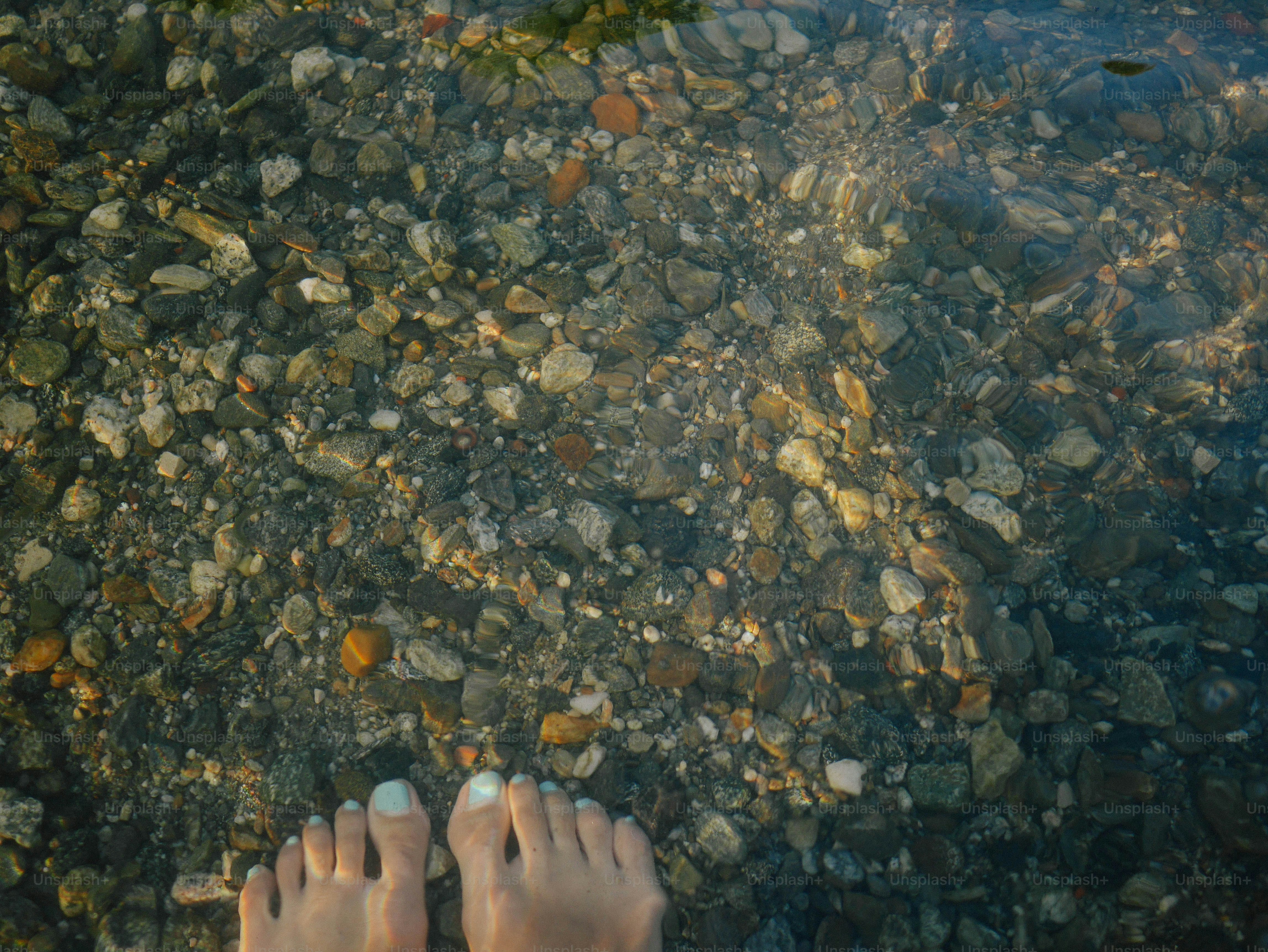 Feet stand over clear water with rocks.