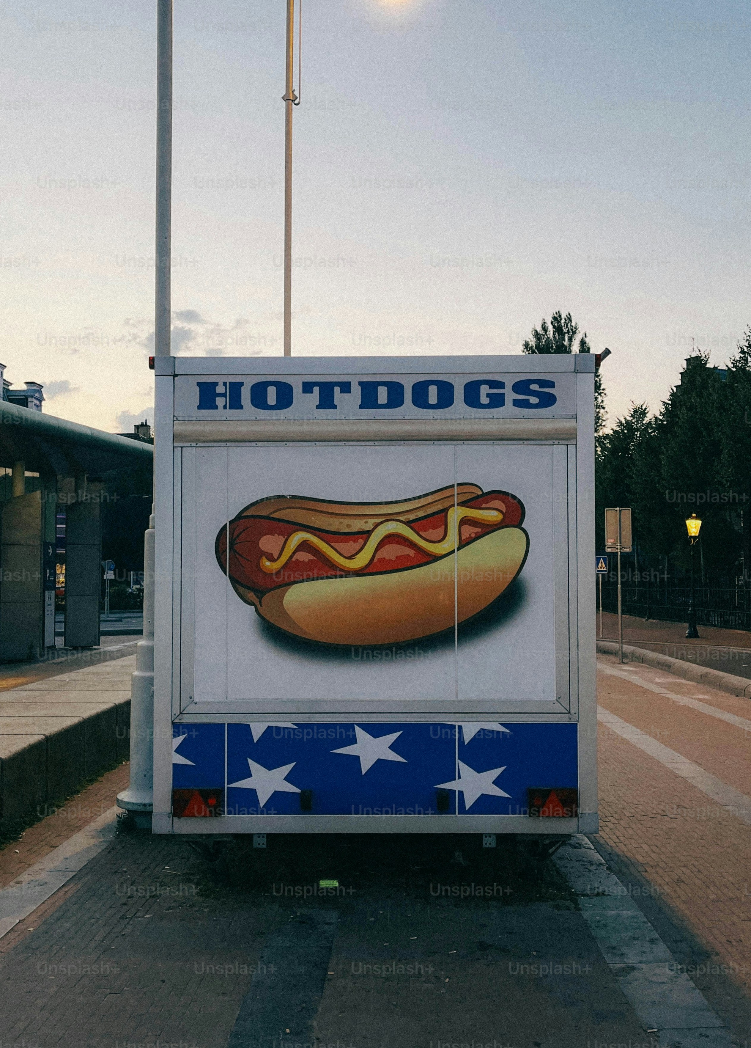 A hot dog stand is parked near a street.