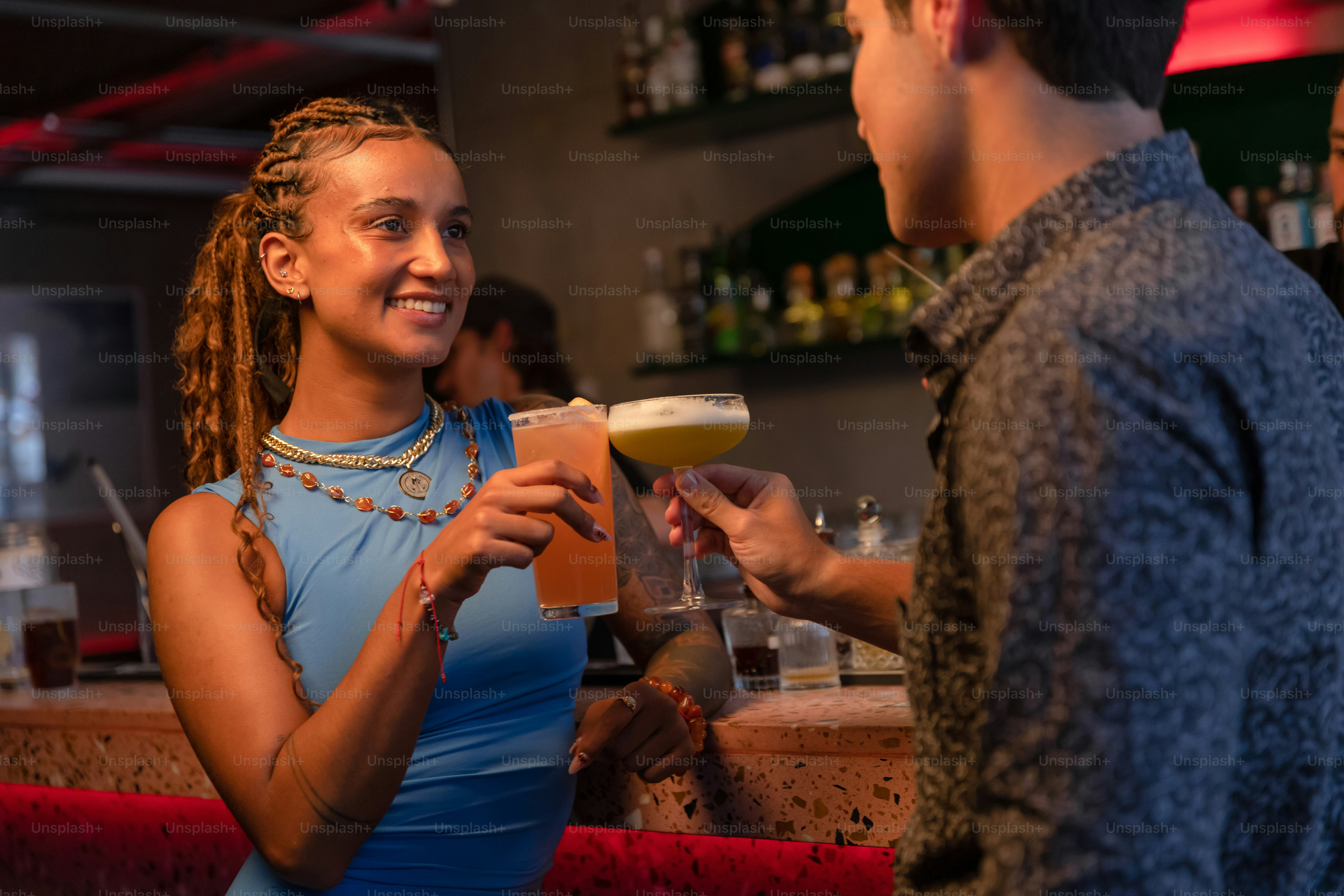 A couple toasts with cocktails at a bar.