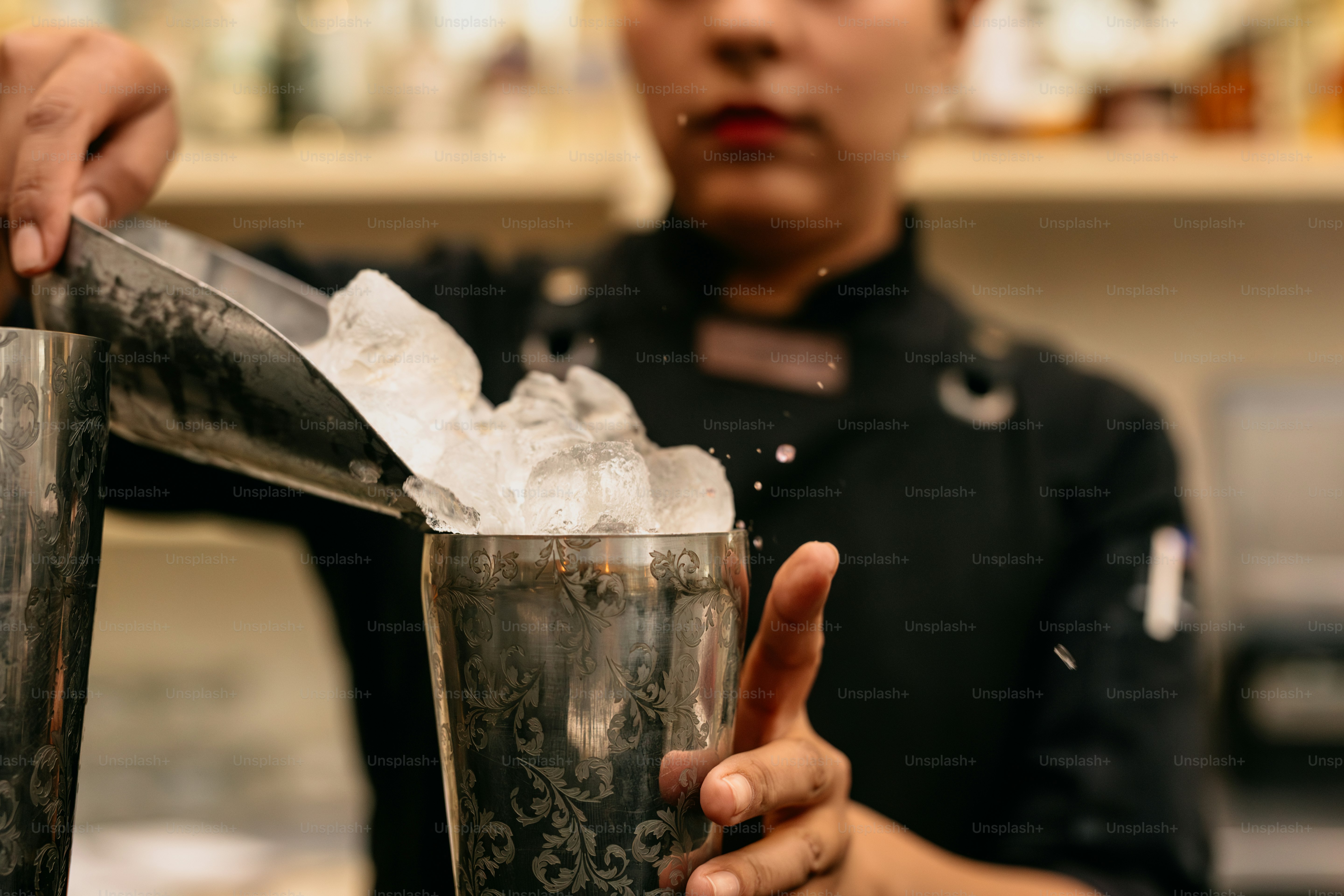 A bartender adds ice to a cocktail shaker.