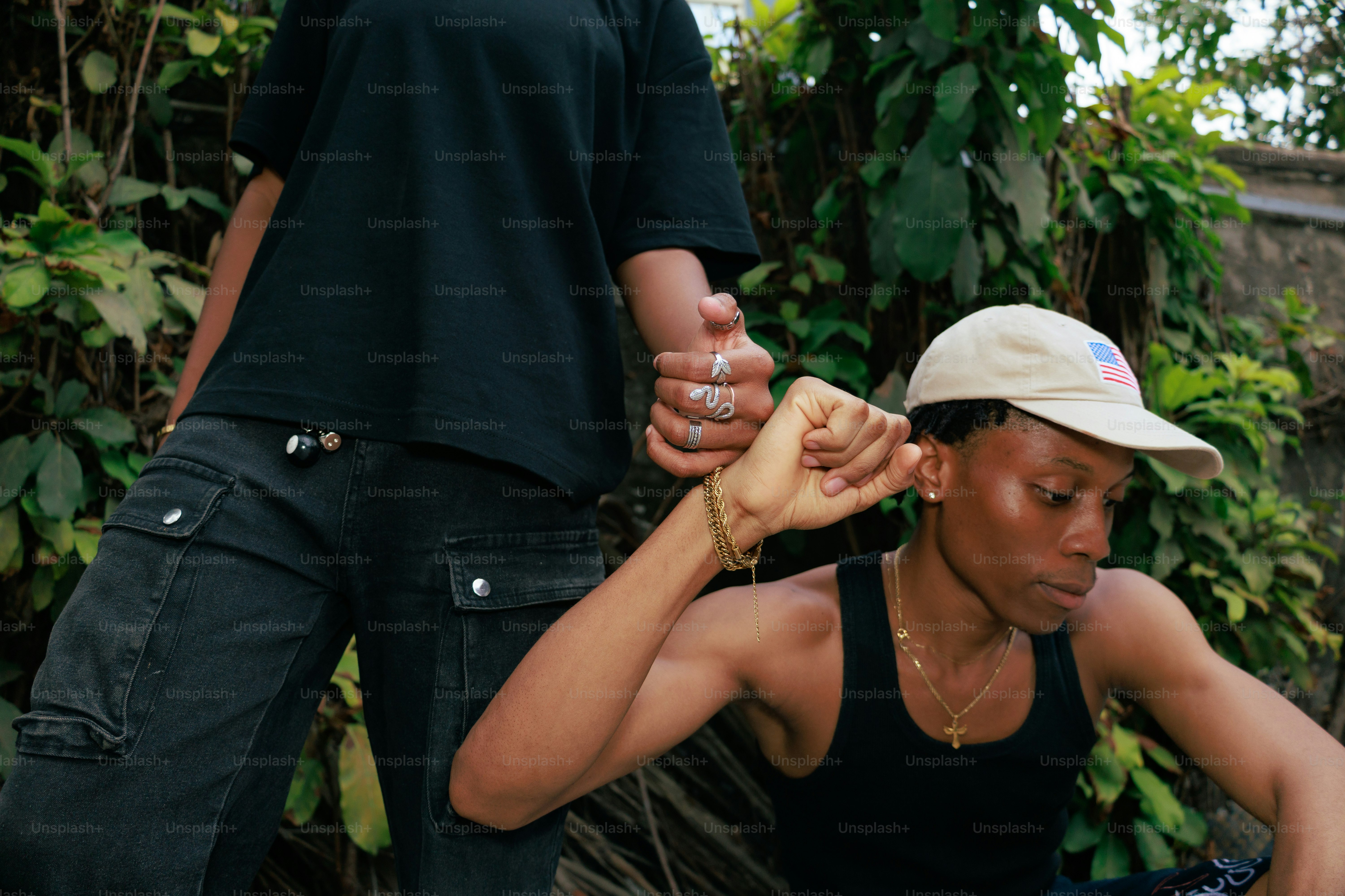 Two people hold hands outdoors surrounded by greenery.