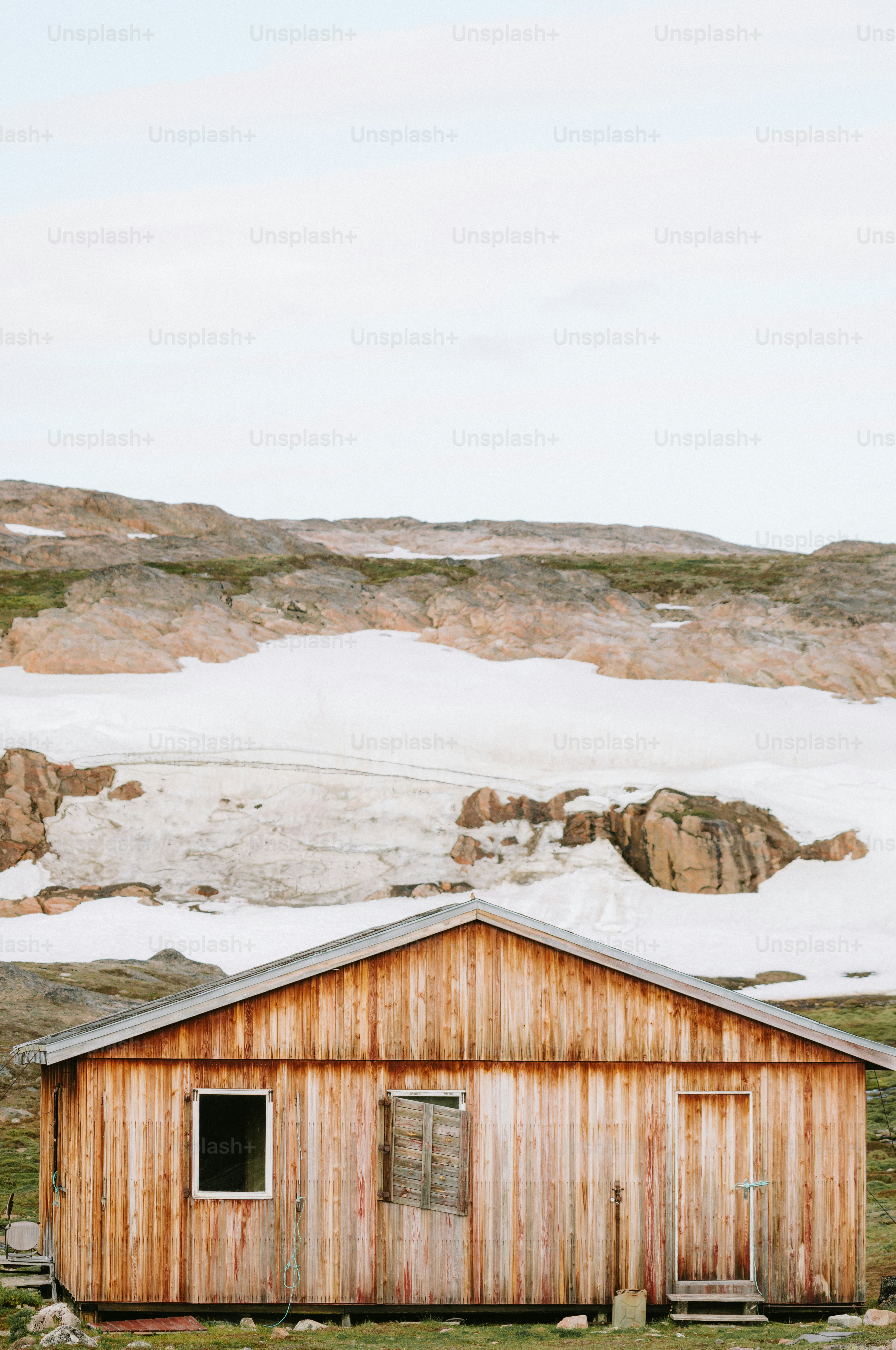 Wooden cabin sits against a snowy mountain backdrop.