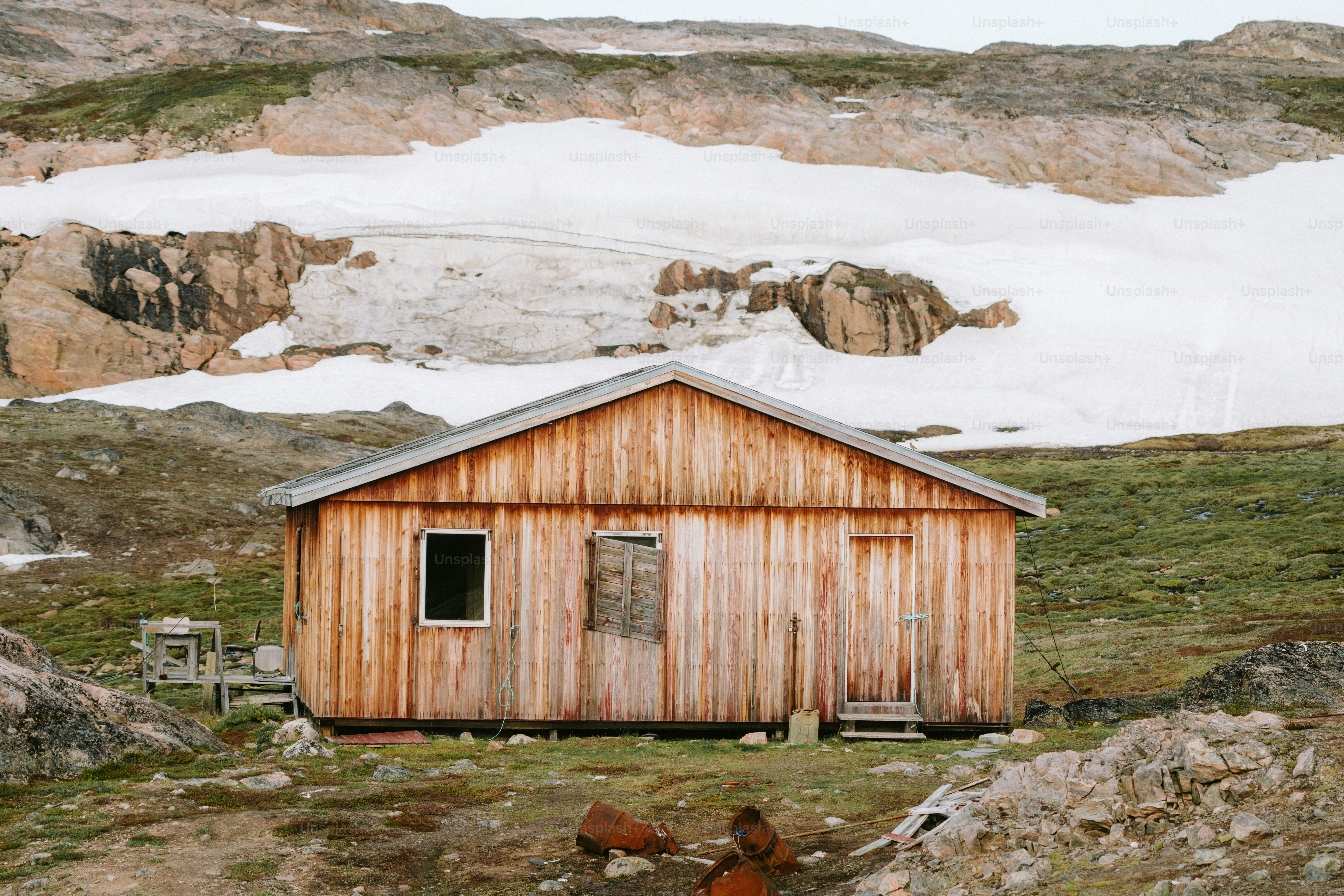 A small wooden cabin stands amidst snowy mountains.