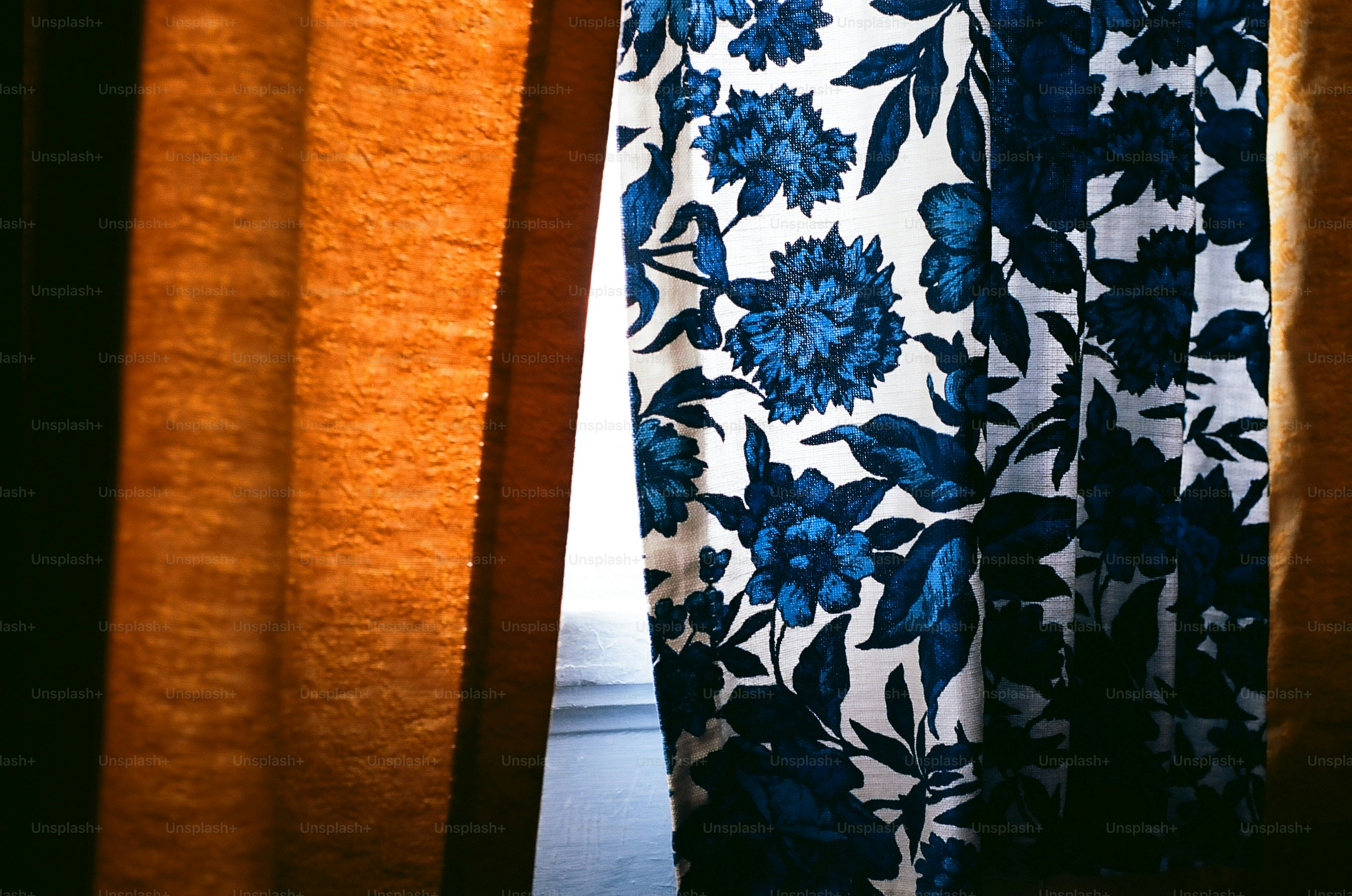 Orange curtains frame floral patterned fabric.