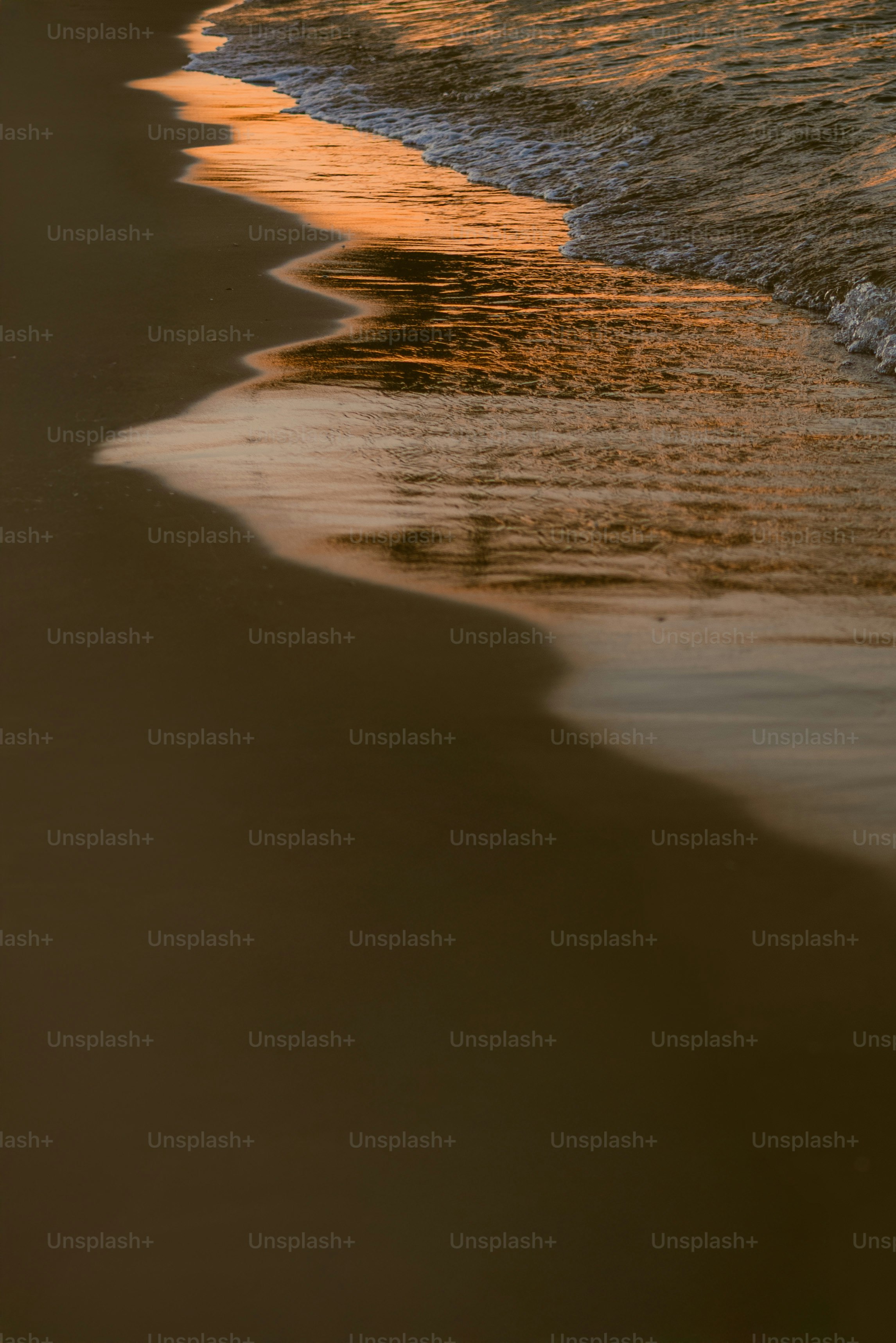 Waves roll onto a sandy beach at sunset.