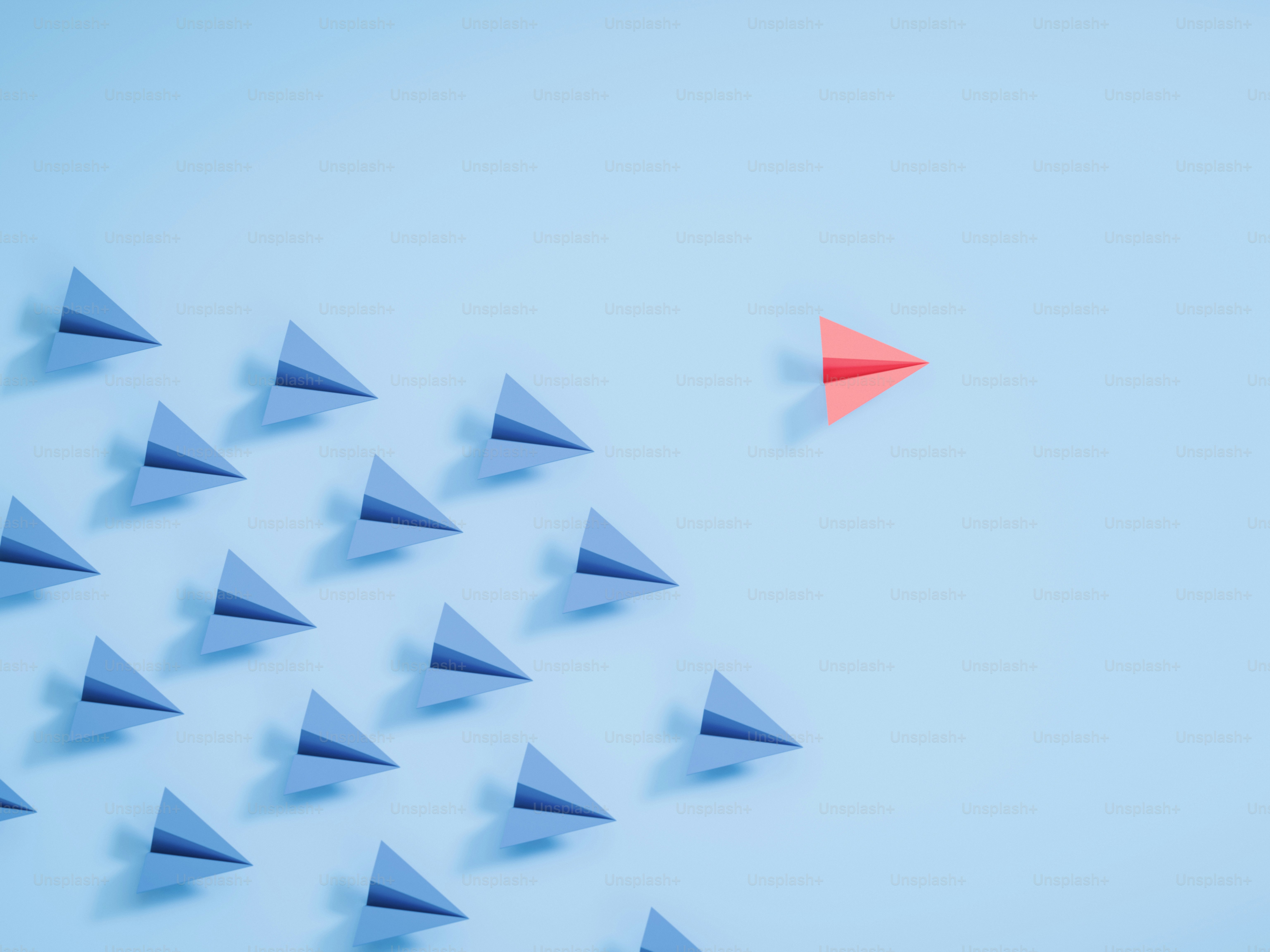 Un avión de papel rojo lidera un grupo de aviones azules.