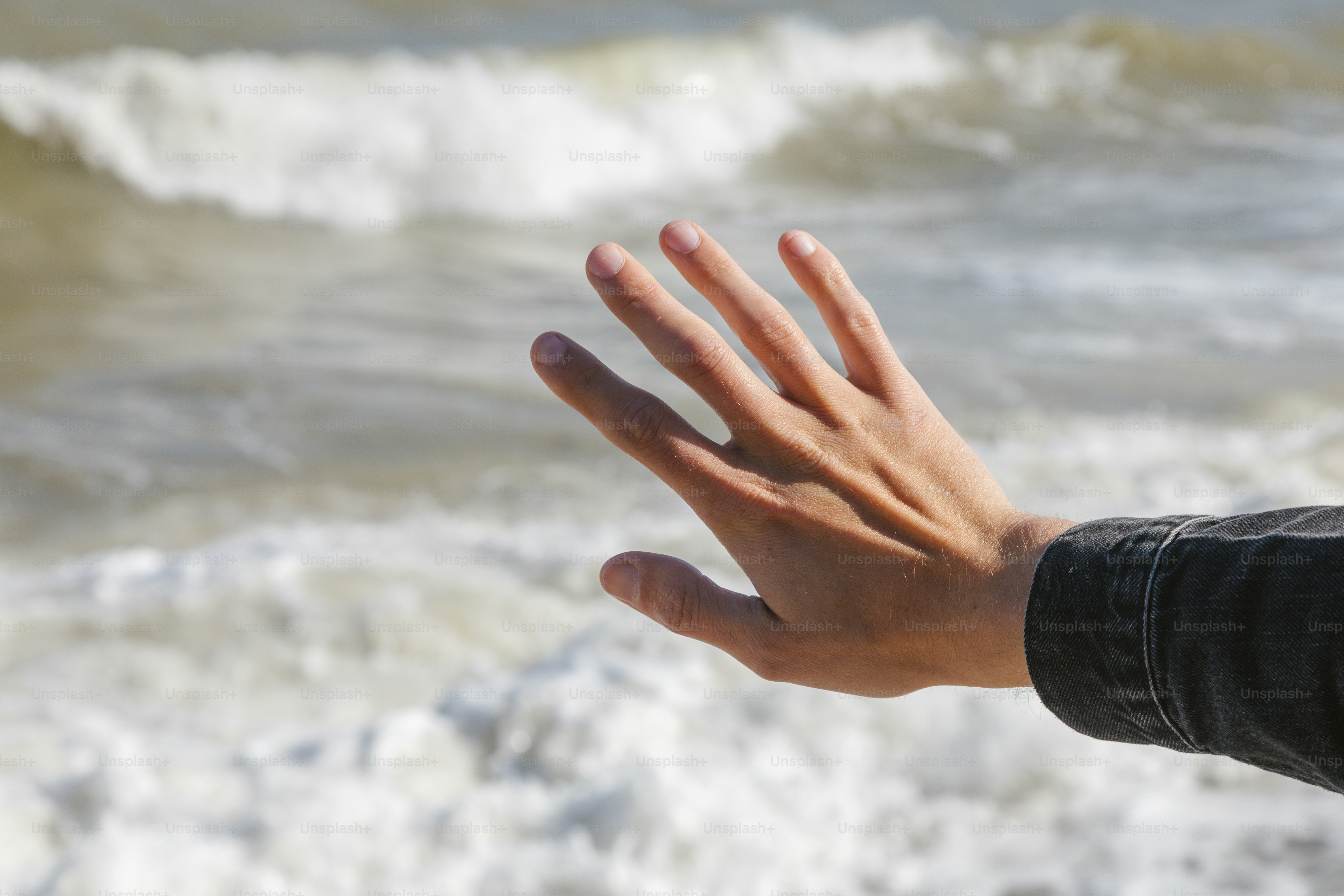 Hand reaches towards the ocean waves. photo – Texture Image on Unsplash