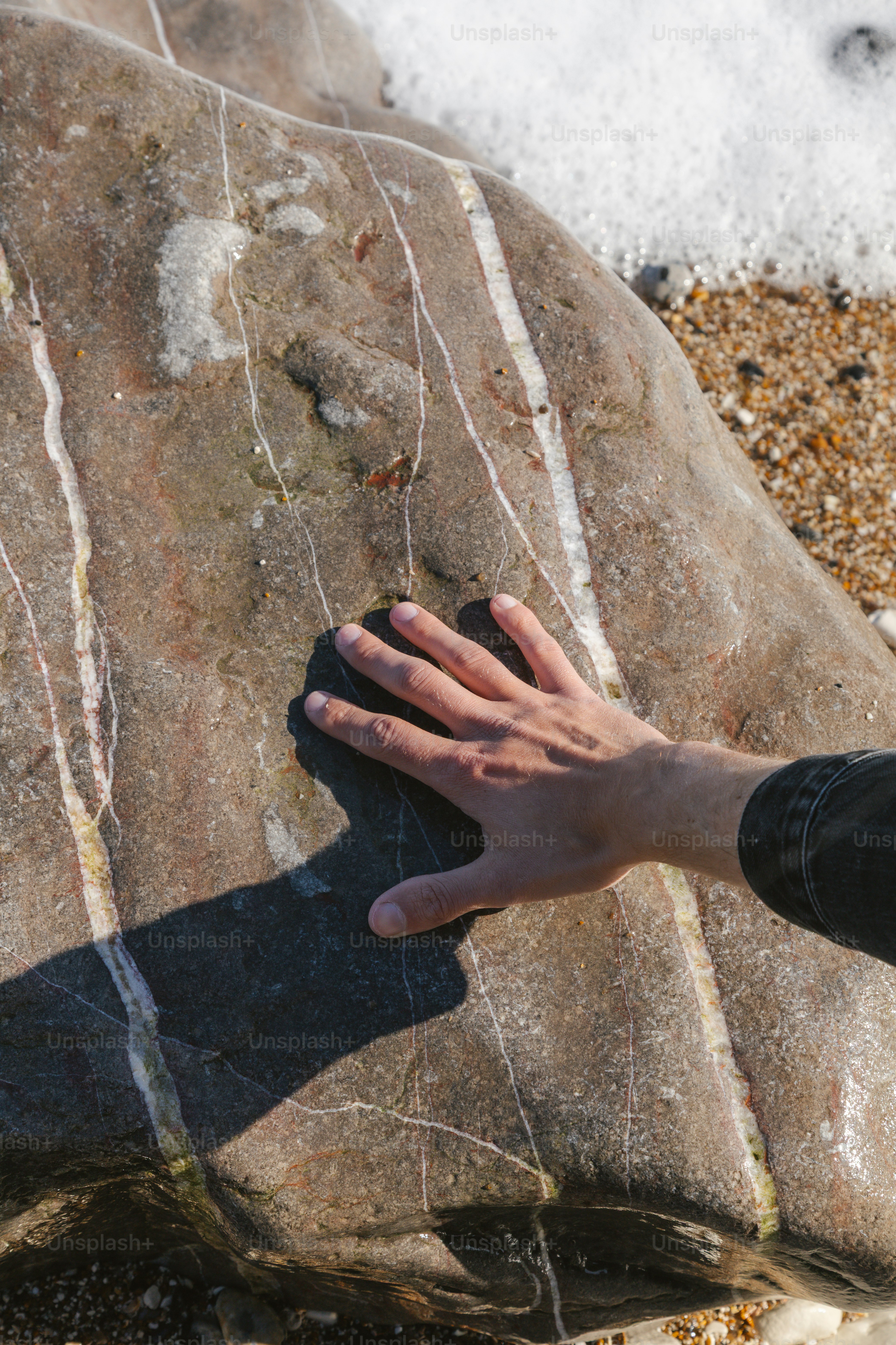 Hand berührt einen gemusterten Stein am Strand.