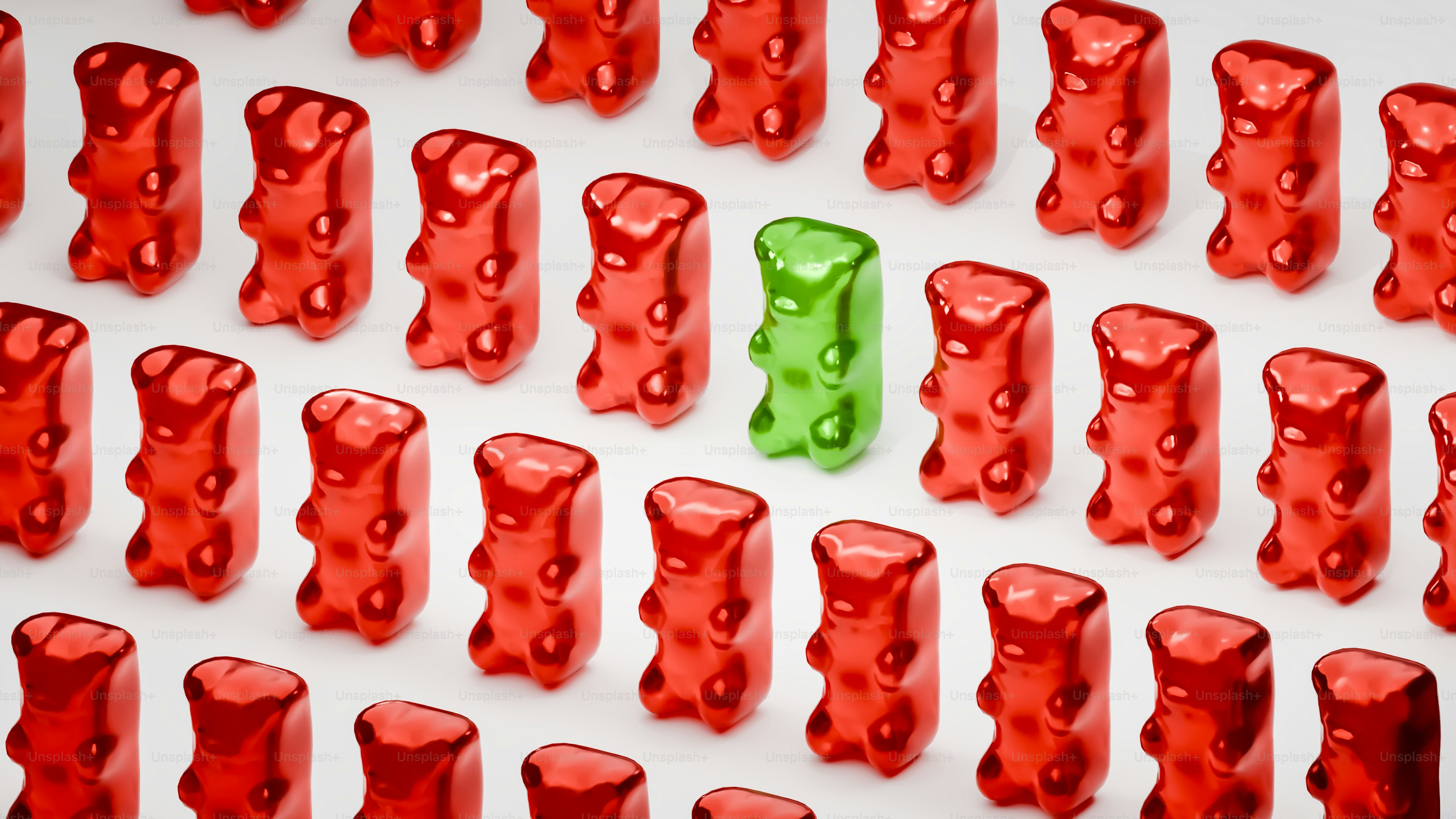 Un osito de goma verde destaca entre muchos rojos.