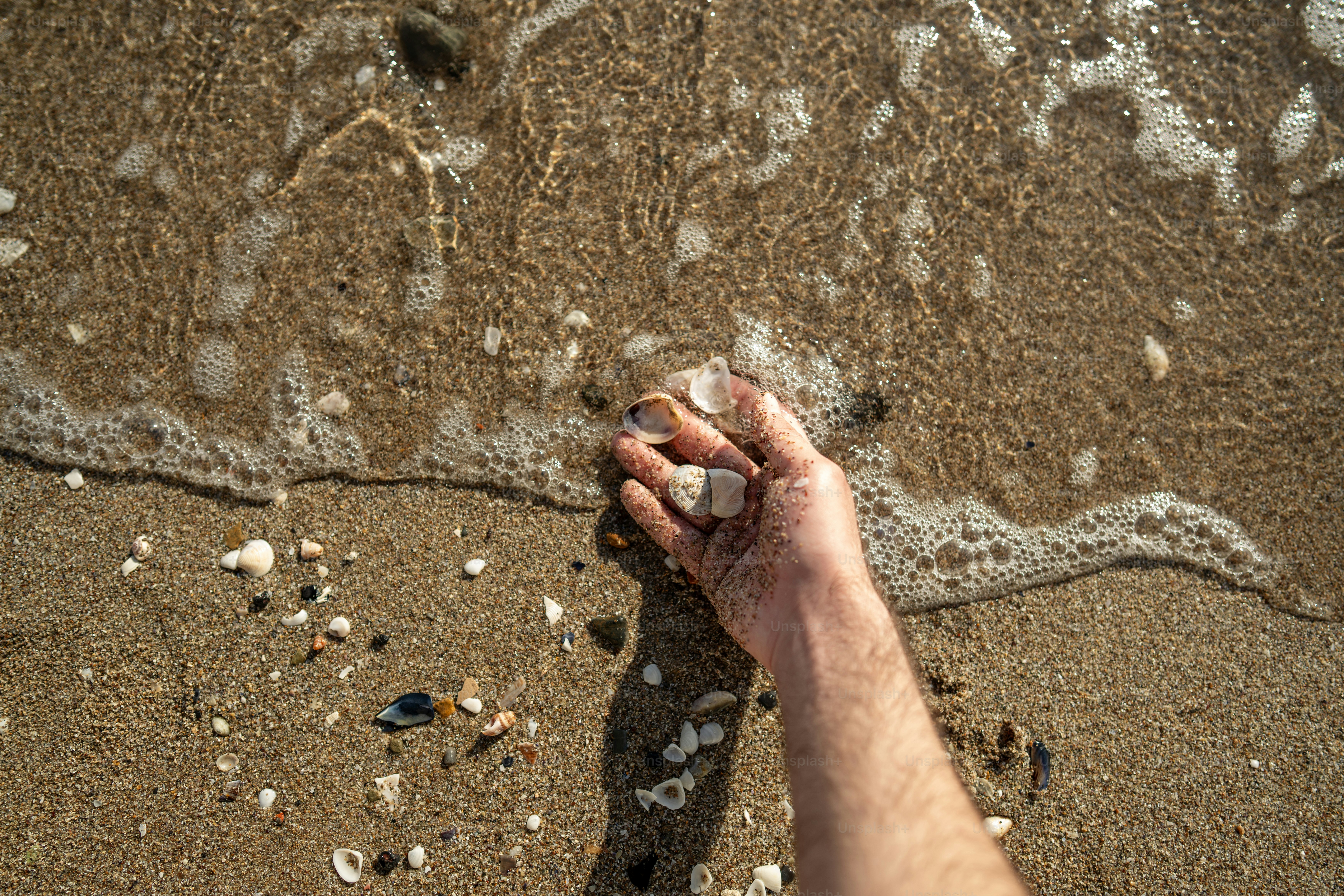 A hand holds pebbles on the sandy beach.
