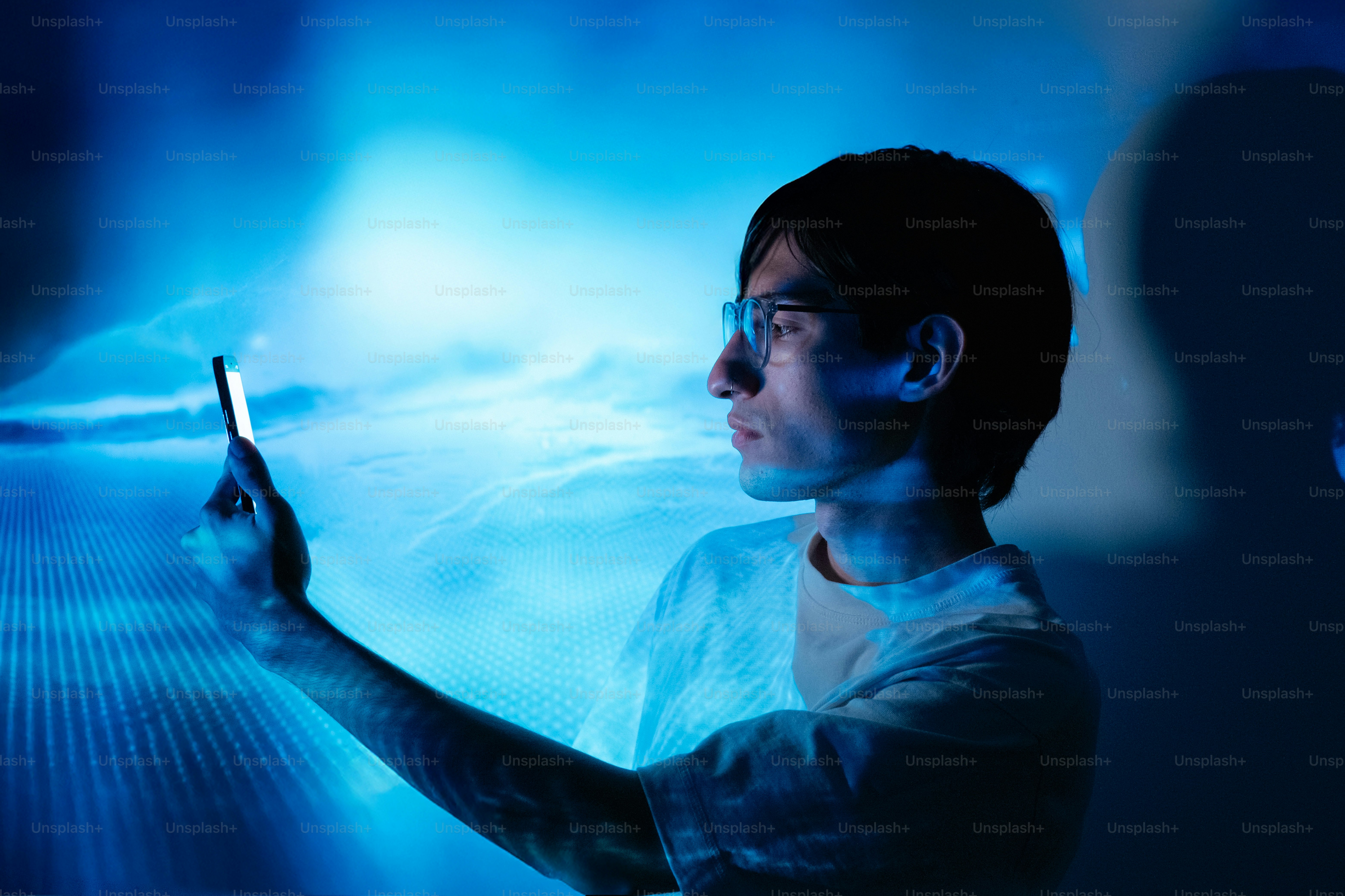 Man looks at his phone in a blue environment.