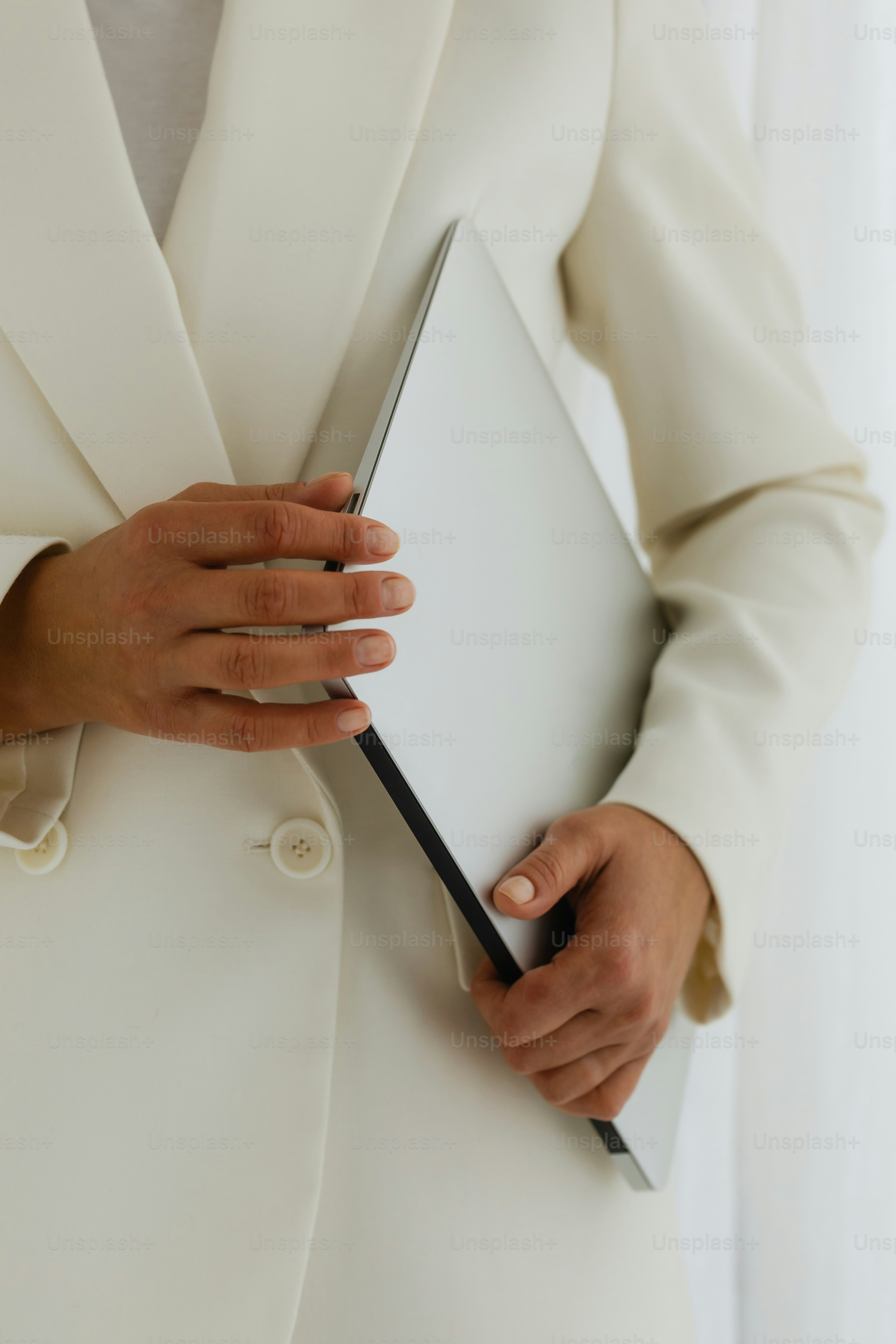 A woman holds a laptop, dressed in a blazer.