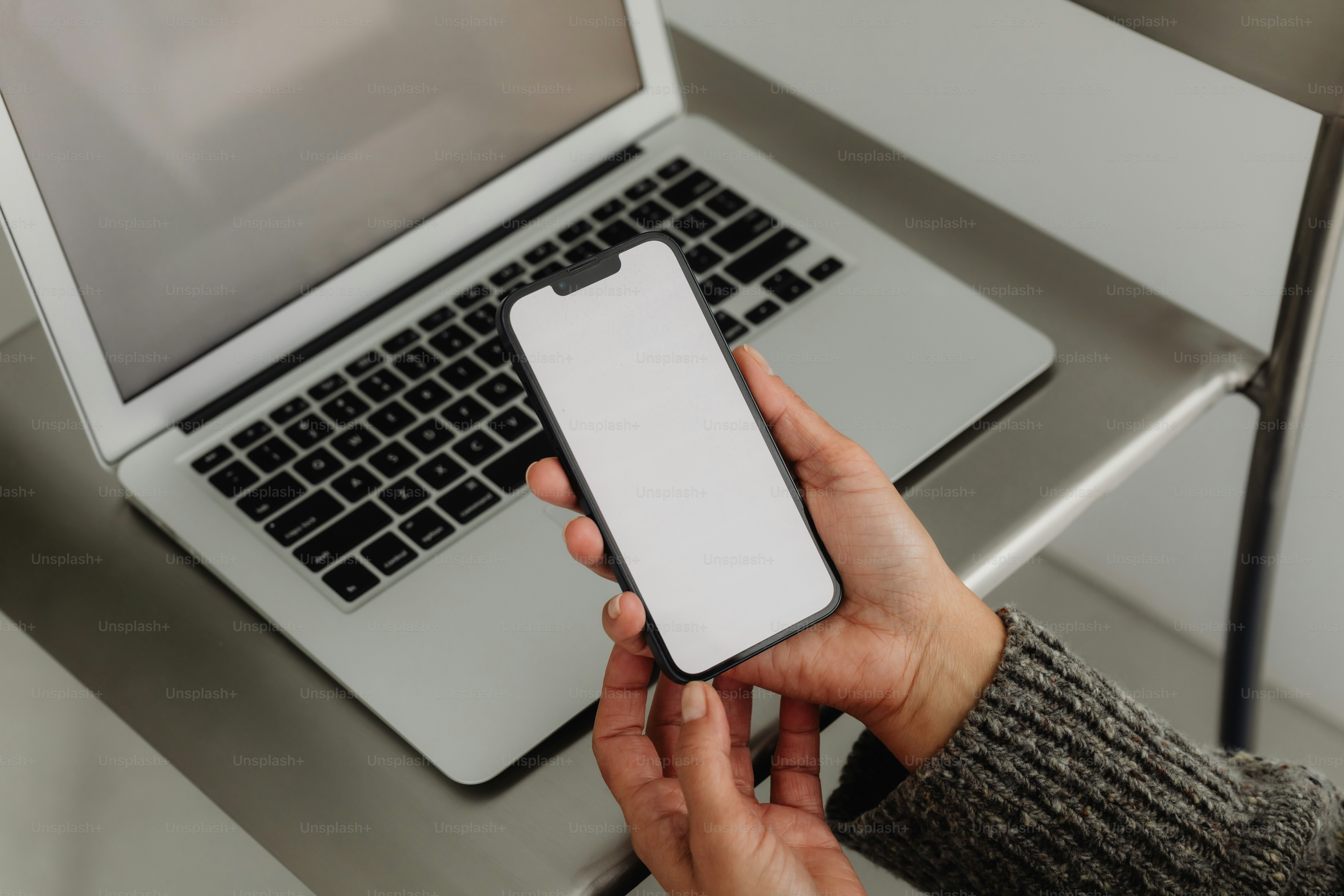 A person holds a phone next to a laptop.