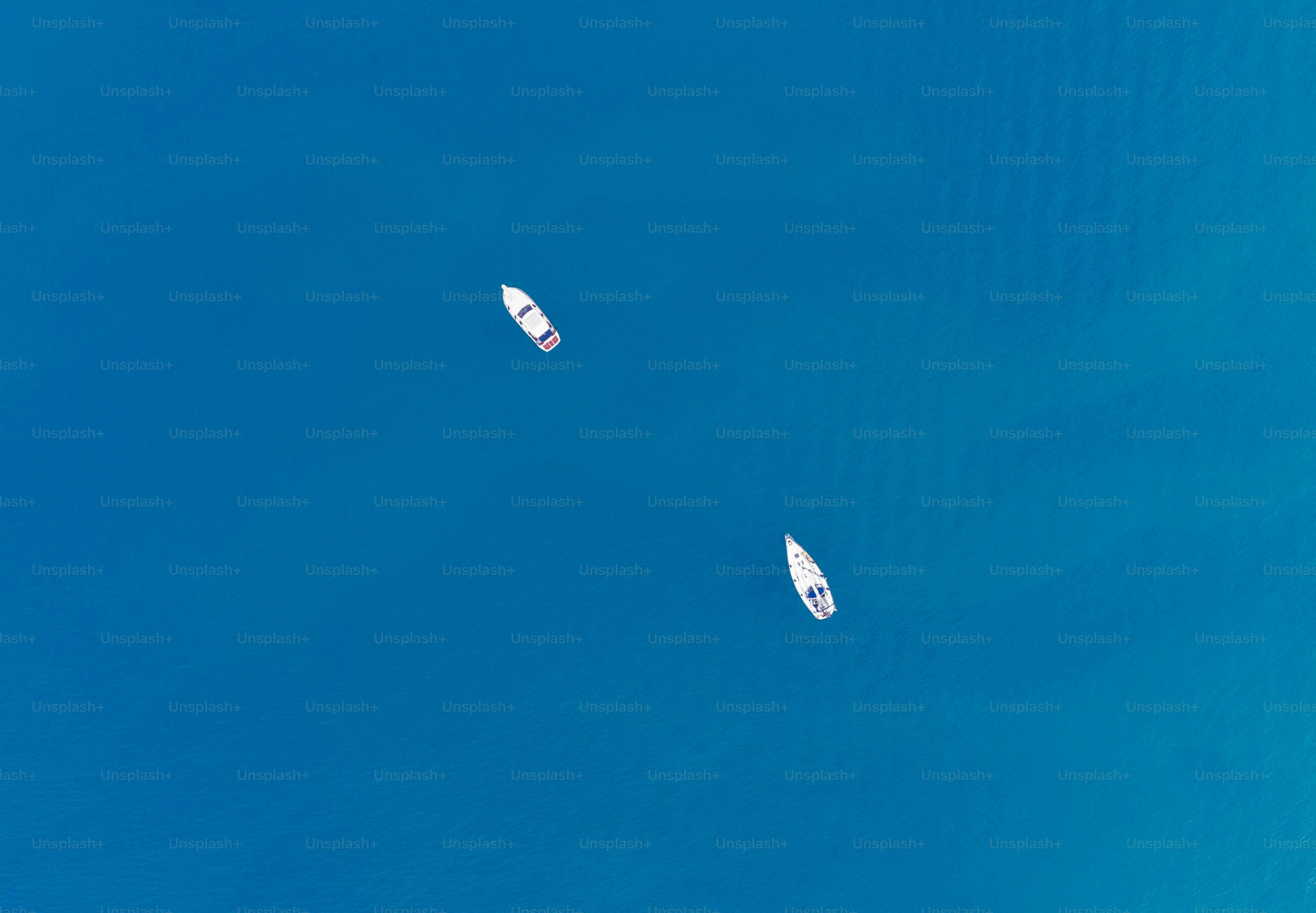 Zwei Segelboote treiben auf einem strahlend blauen Meer.