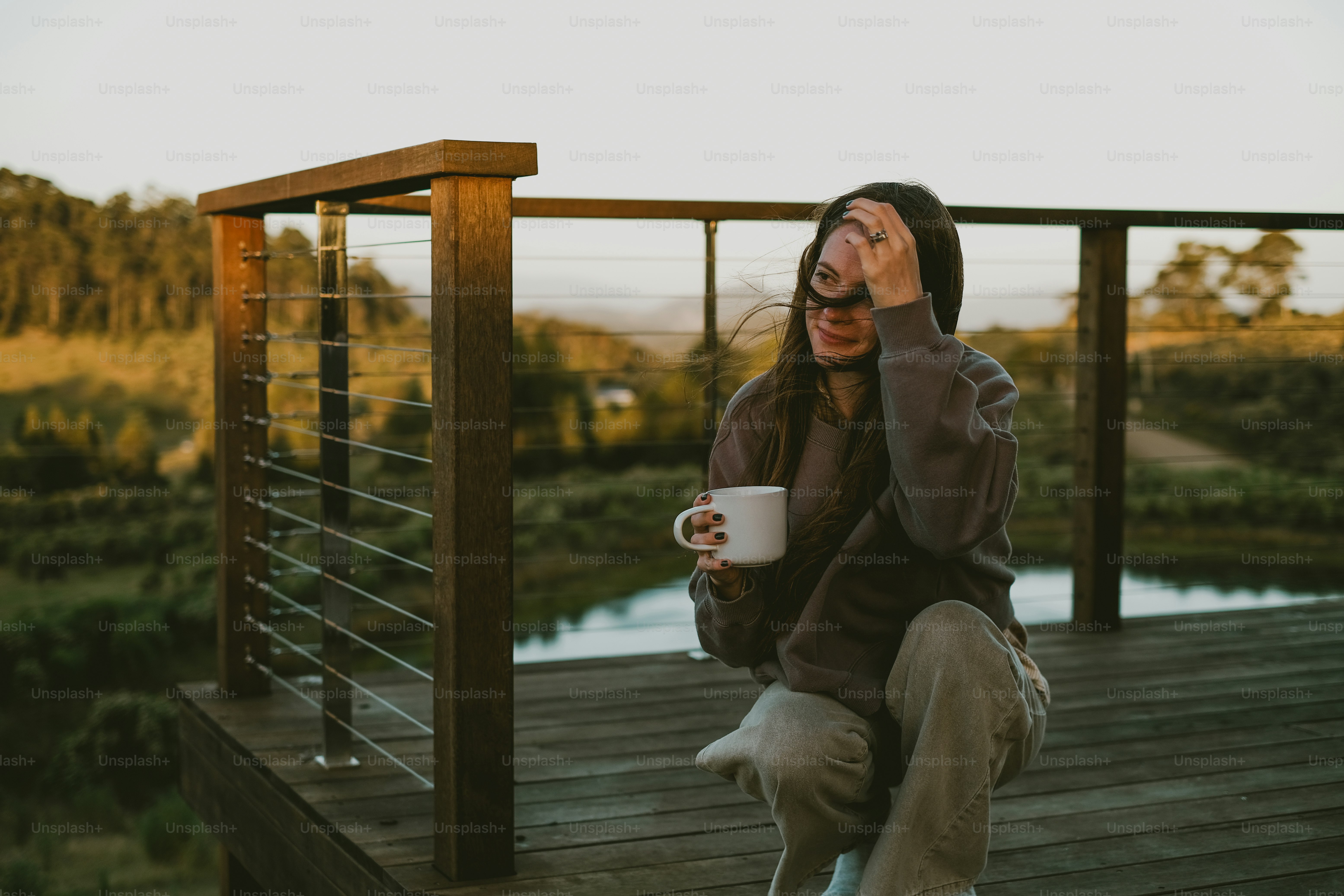Woman enjoys coffee on a deck overlooking a scenic view.