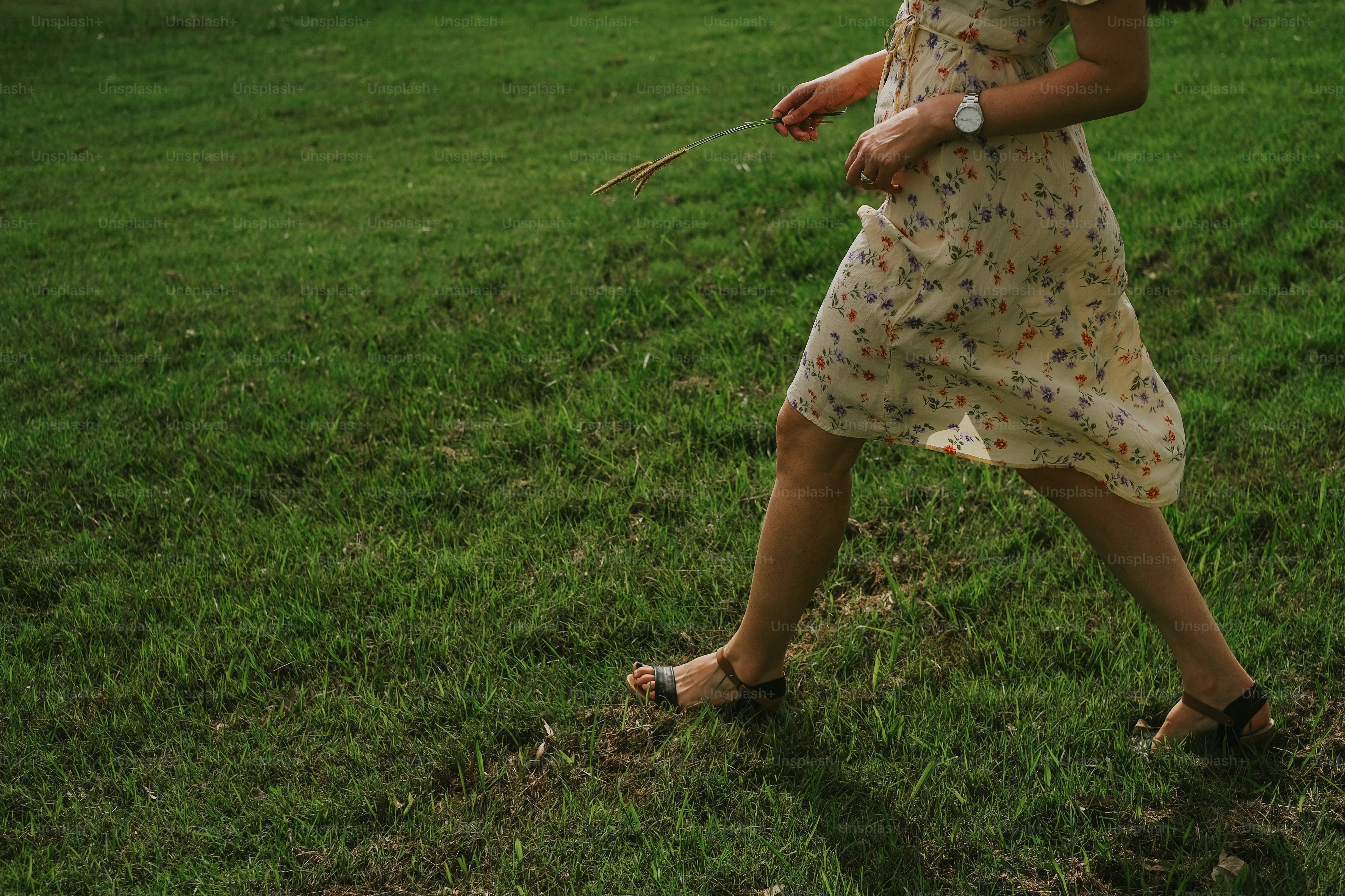 Woman walking on the grass, holding a twig.