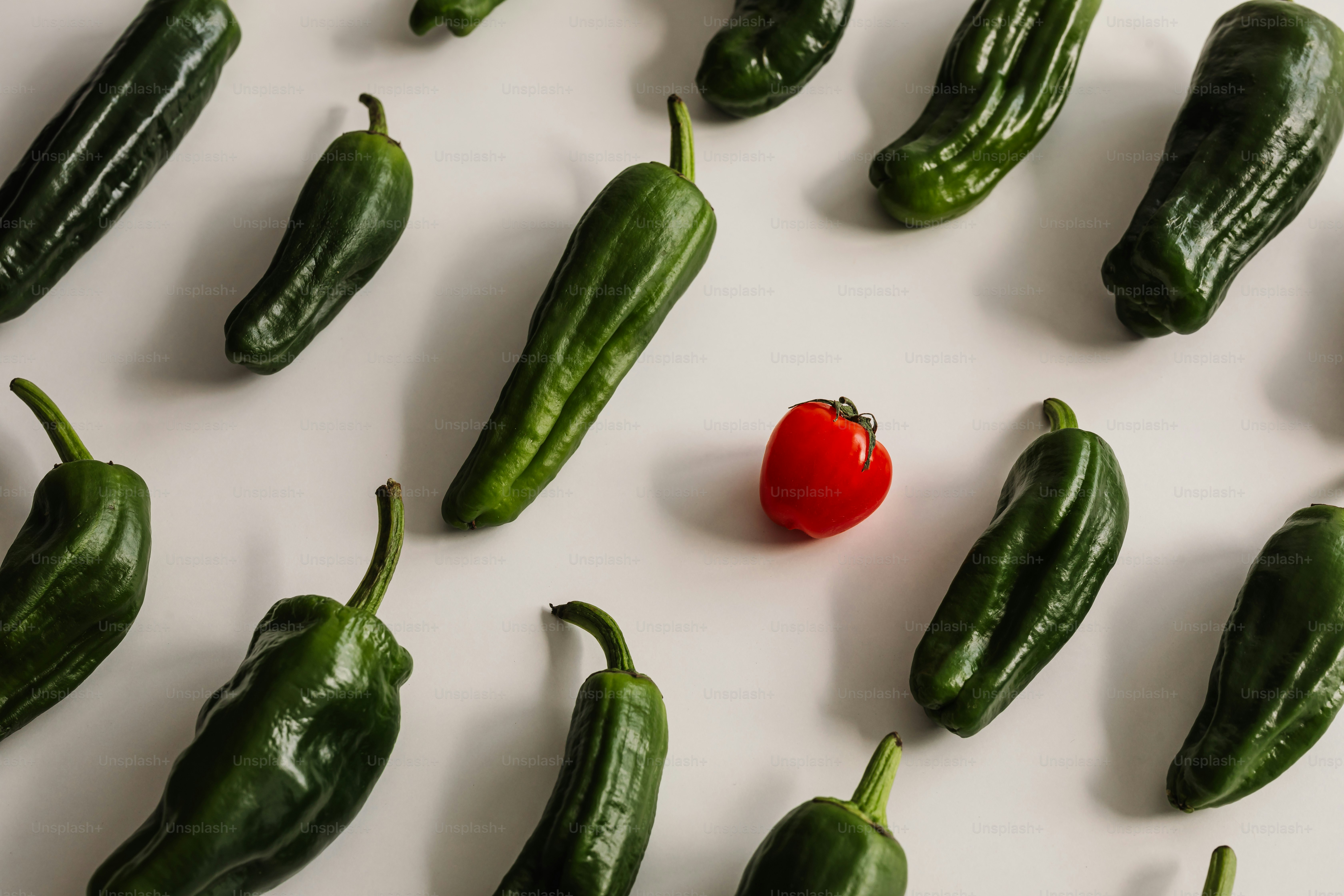 Green peppers are arranged with a single red one.