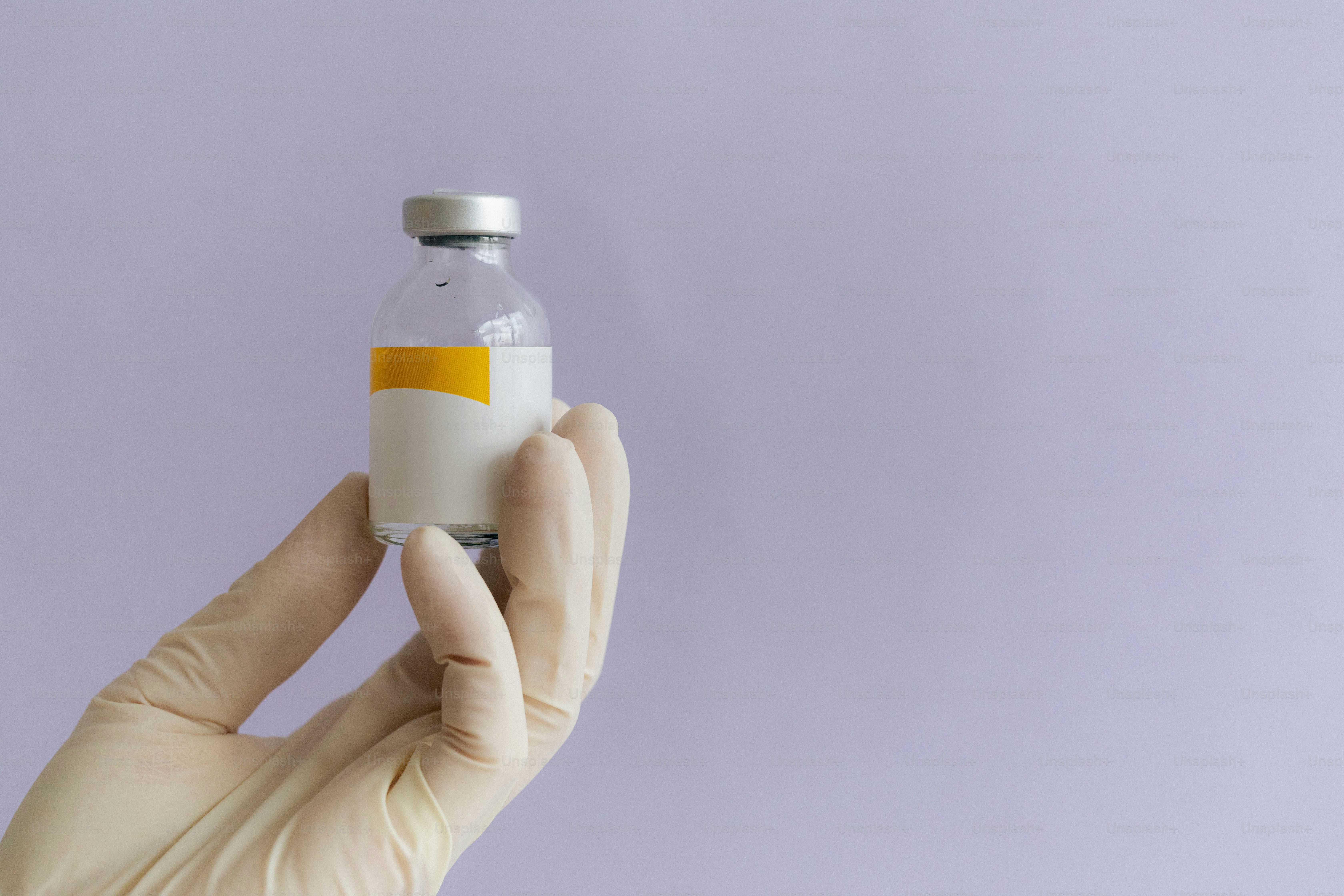 A gloved hand holds a vial of medicine.