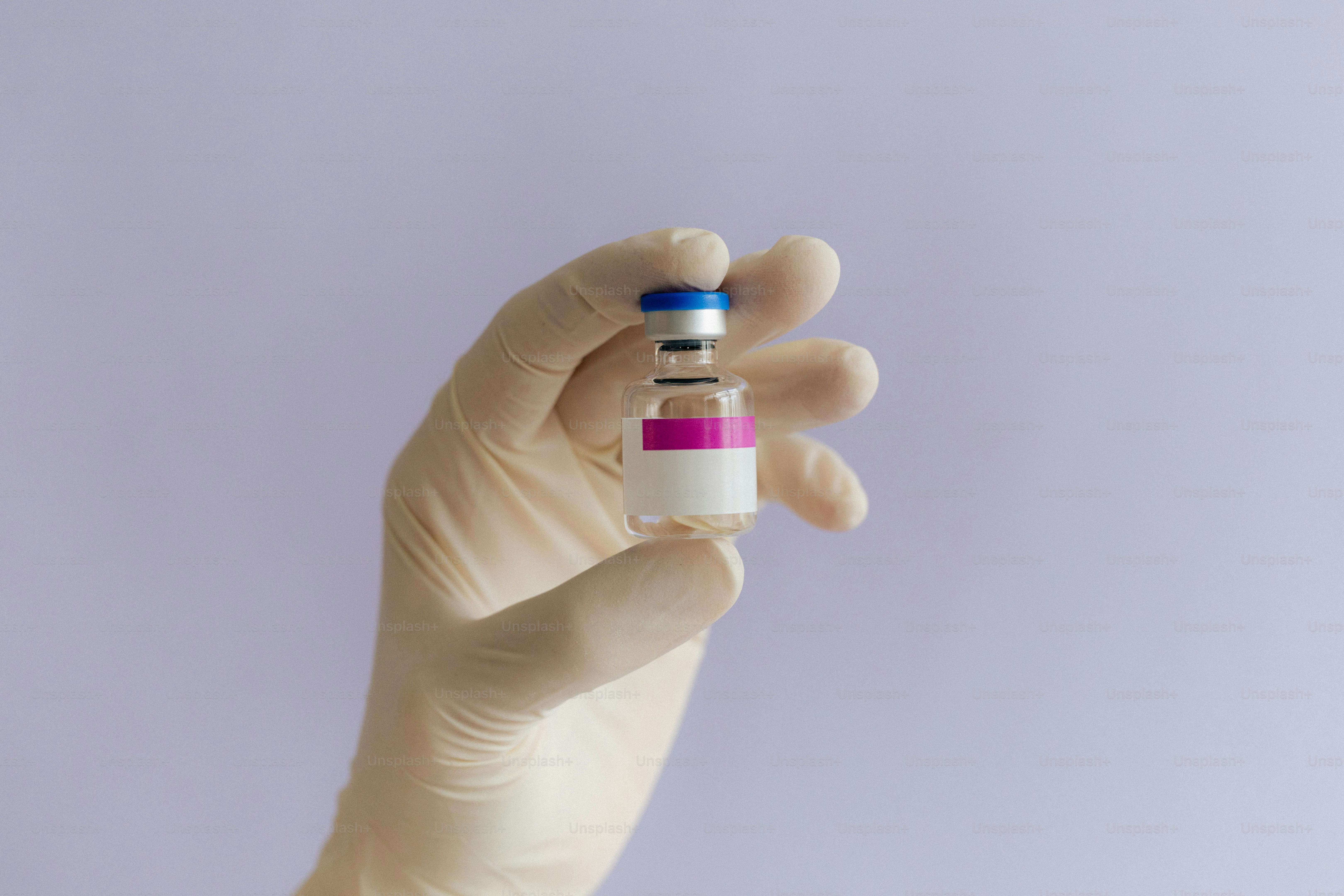 A hand in a glove holds a vaccine vial.