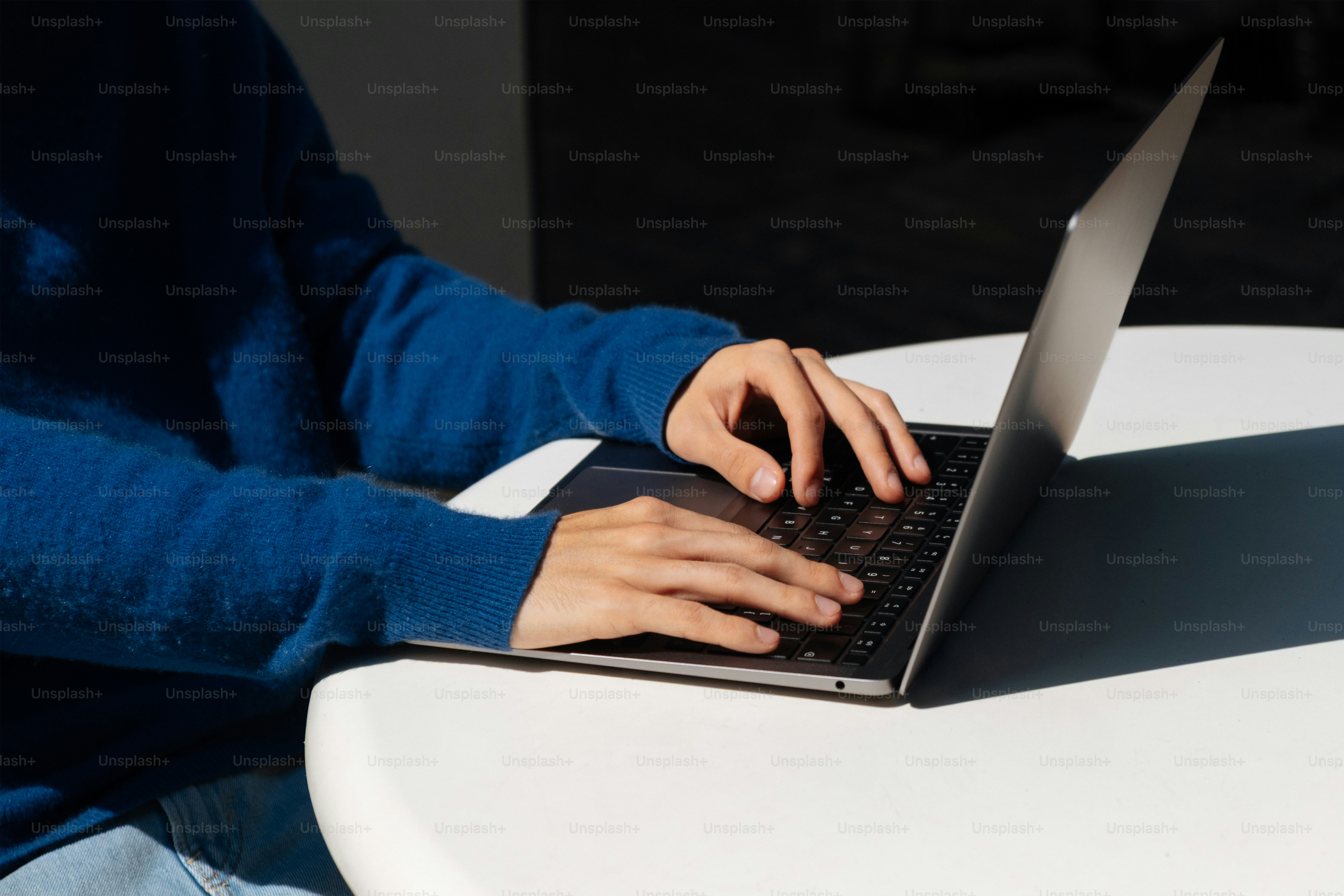 Person types on a laptop with blue sweater.