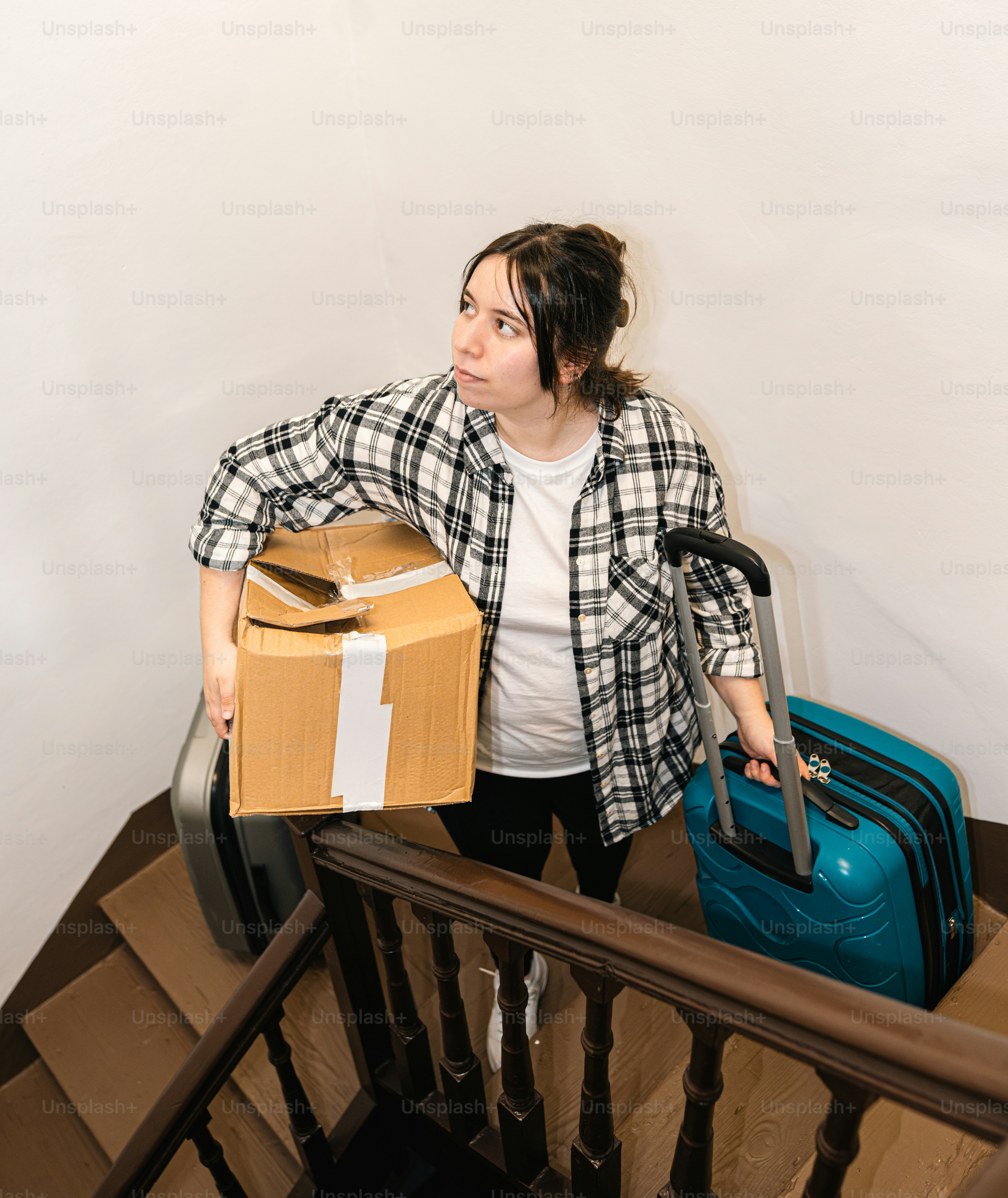 Woman carries boxes and a suitcase up the stairs.