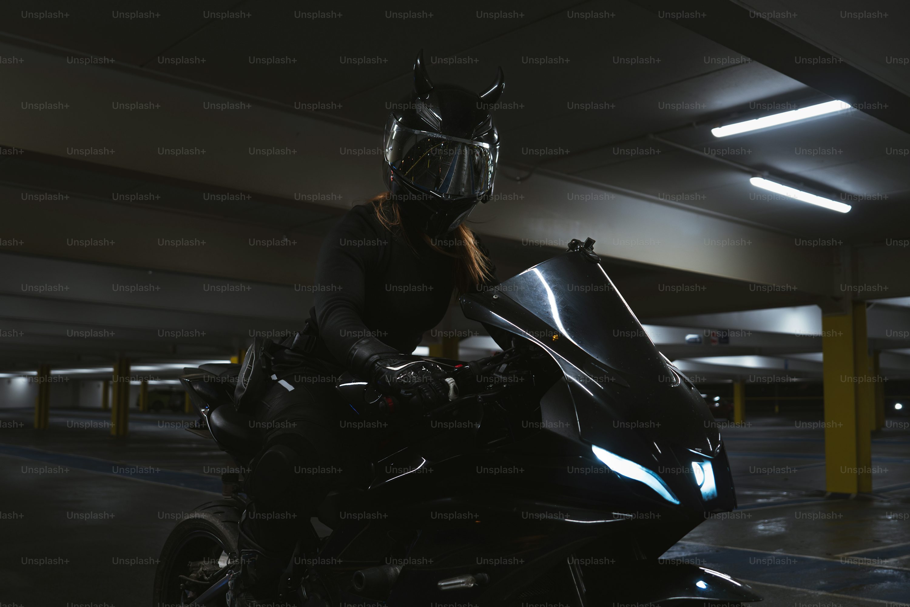 A rider on a motorcycle in a dark parking garage.