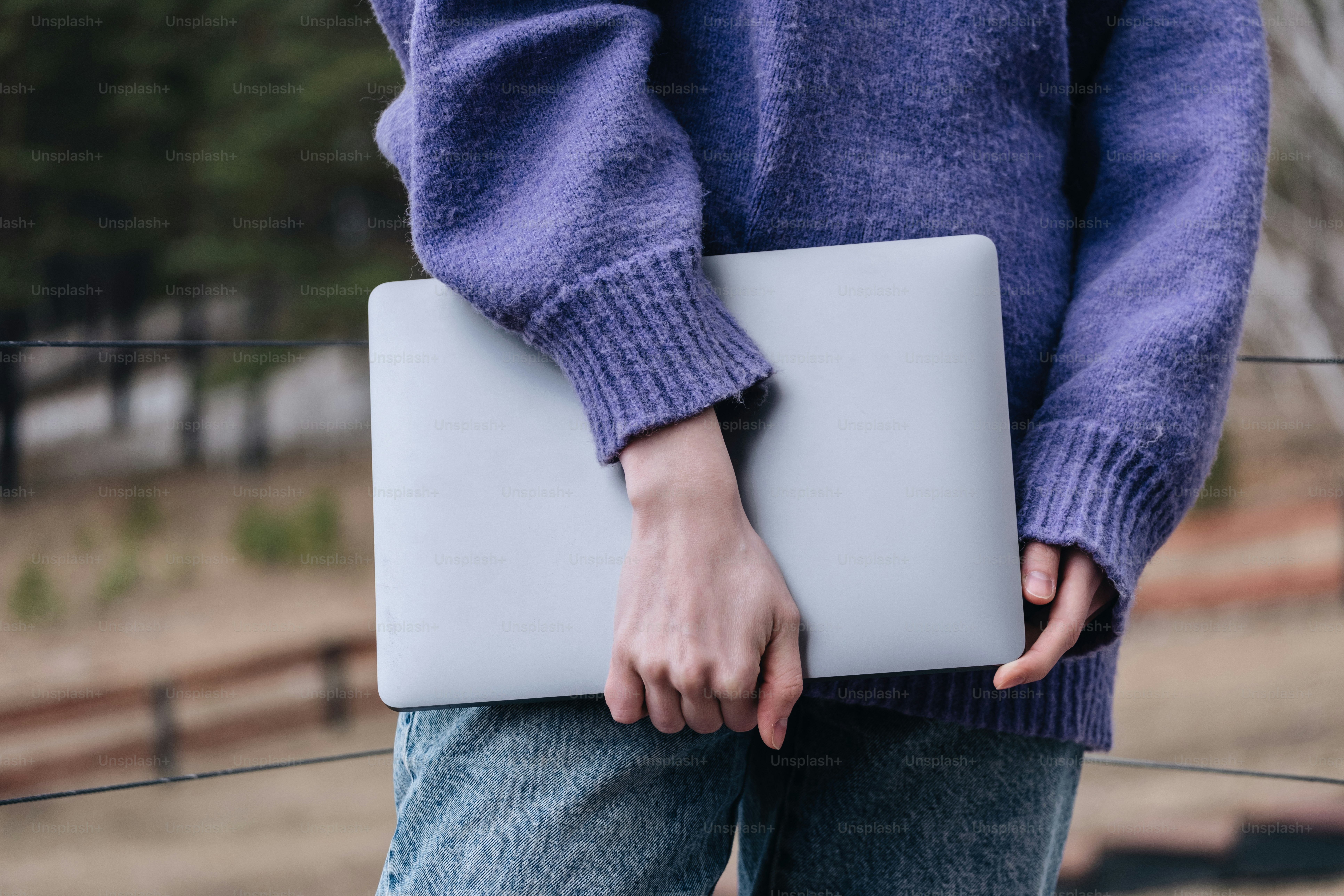 Person holds a laptop wearing a purple sweater.