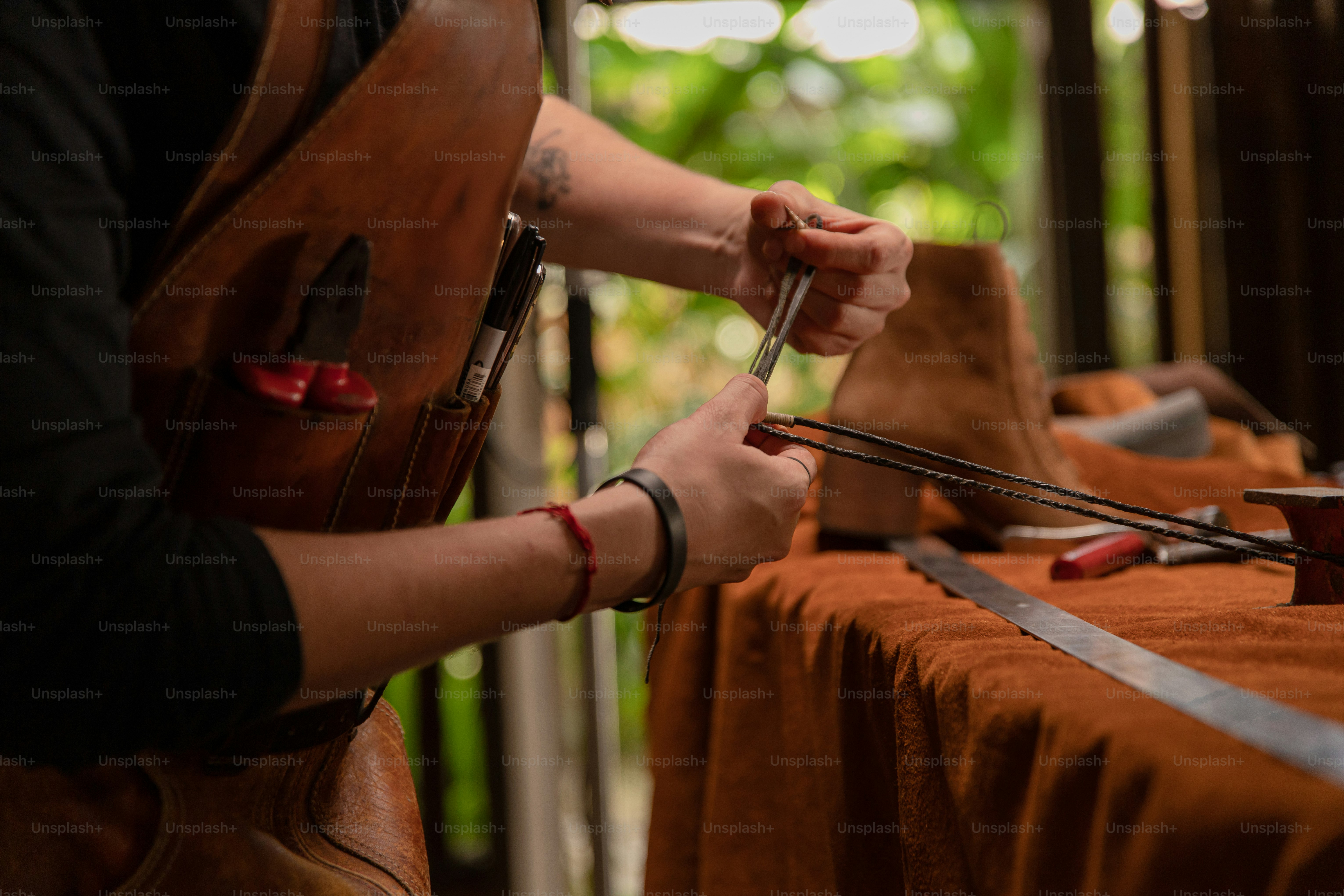 Eine Person näht Leder, während sie eine Schürze trägt.