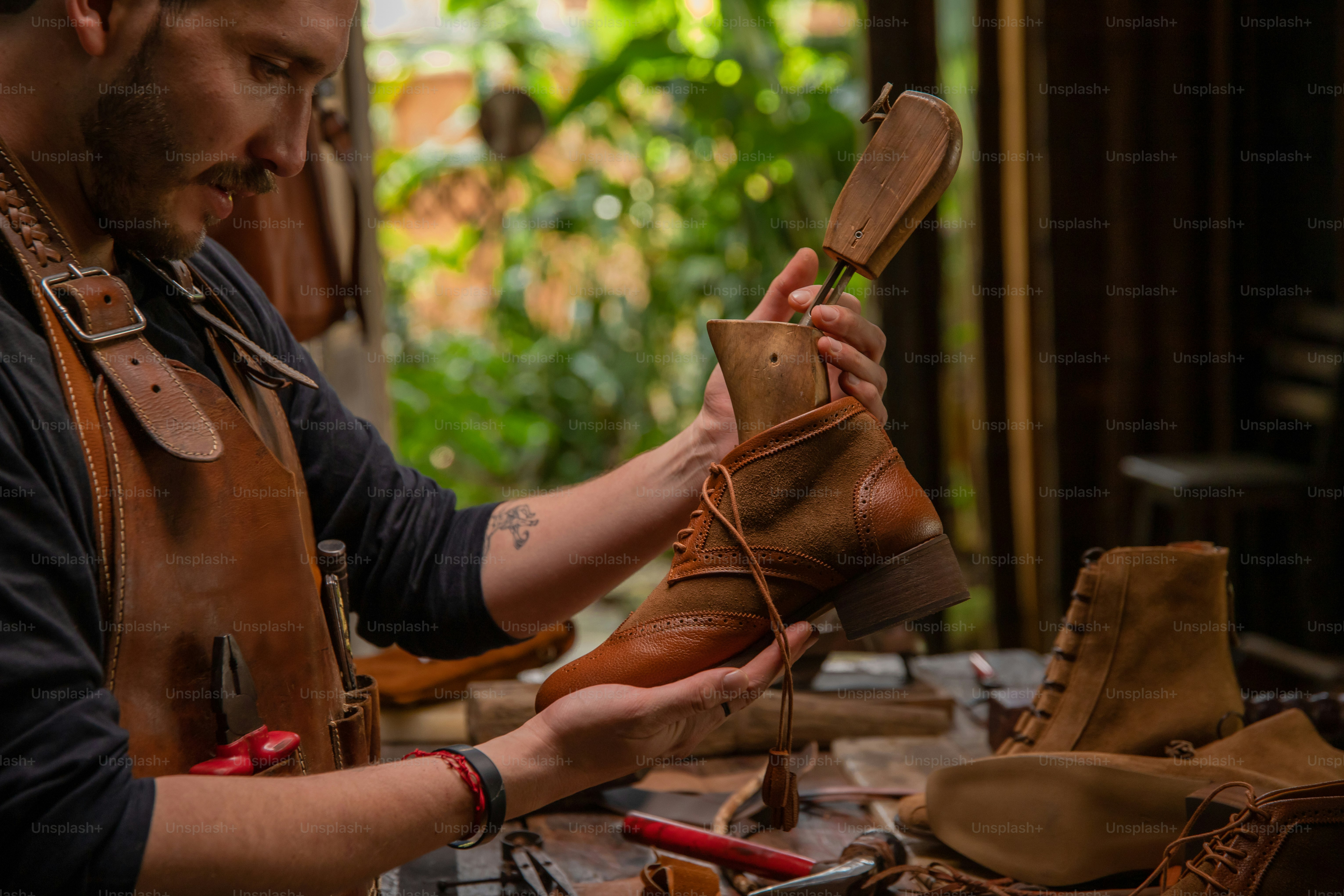 Seorang pembuat sepatu sedang mengerjakan sepatu bot kulit.