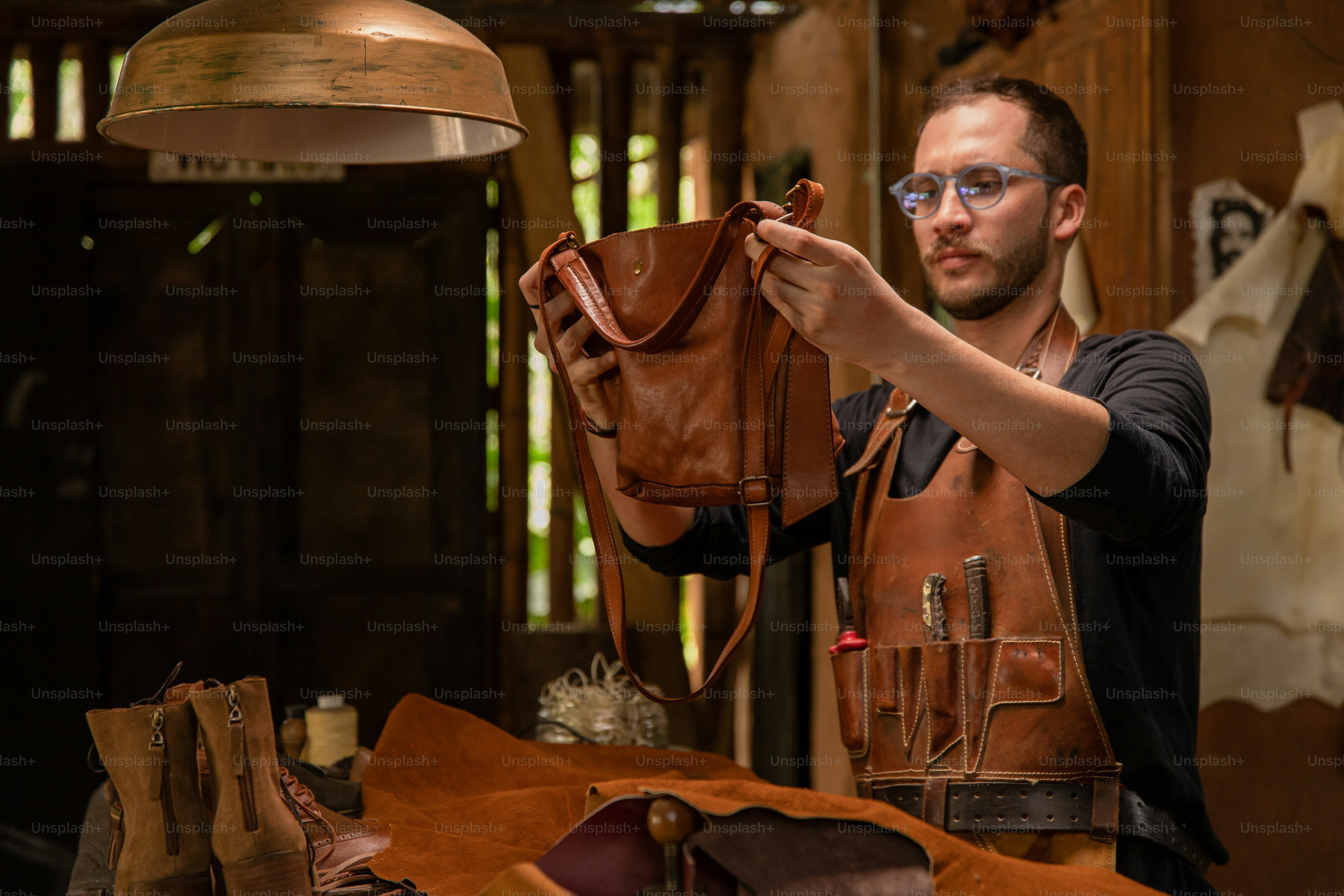A leatherworker is inspecting a brown leather bag.