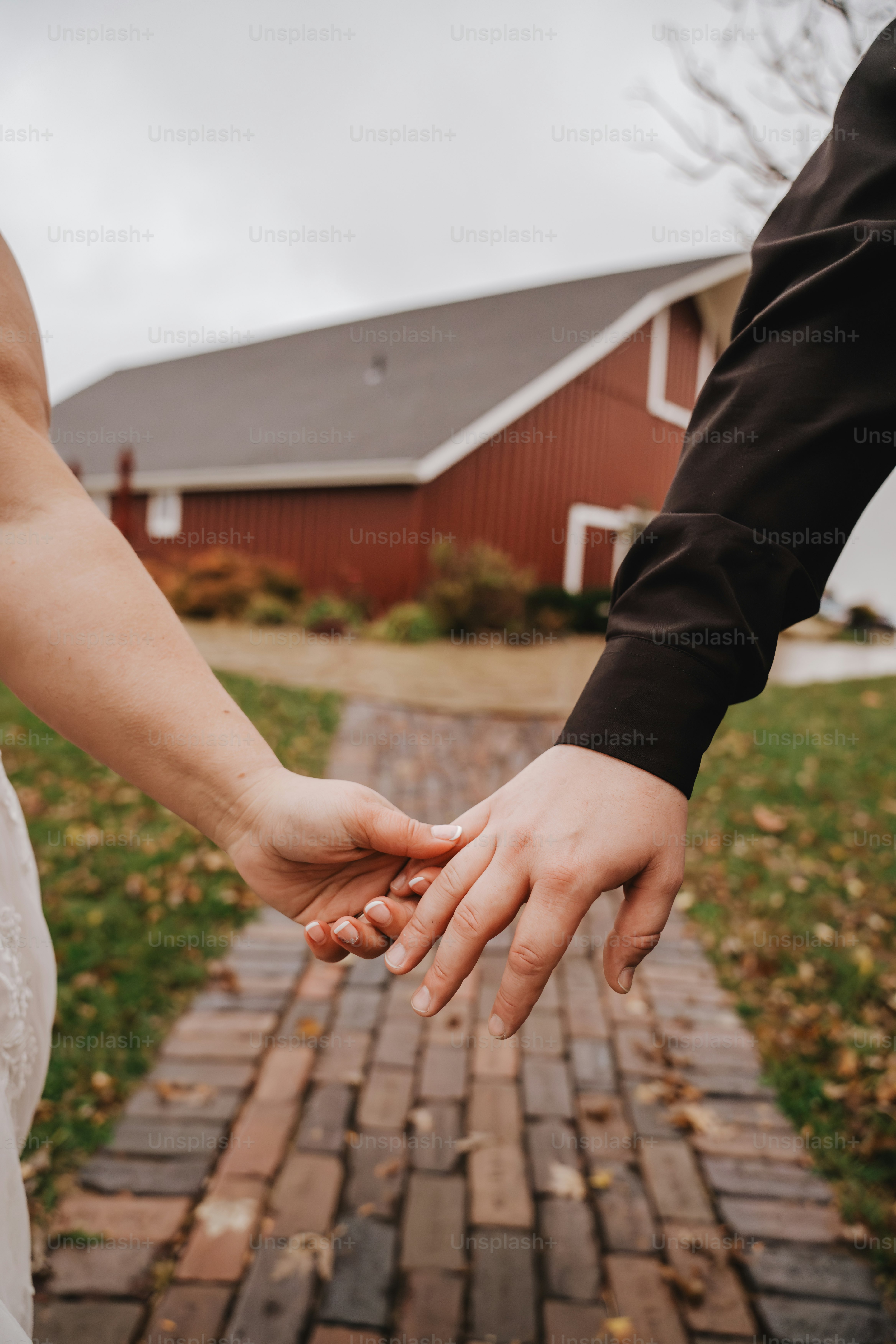 A couple holds hands in front of a barn.