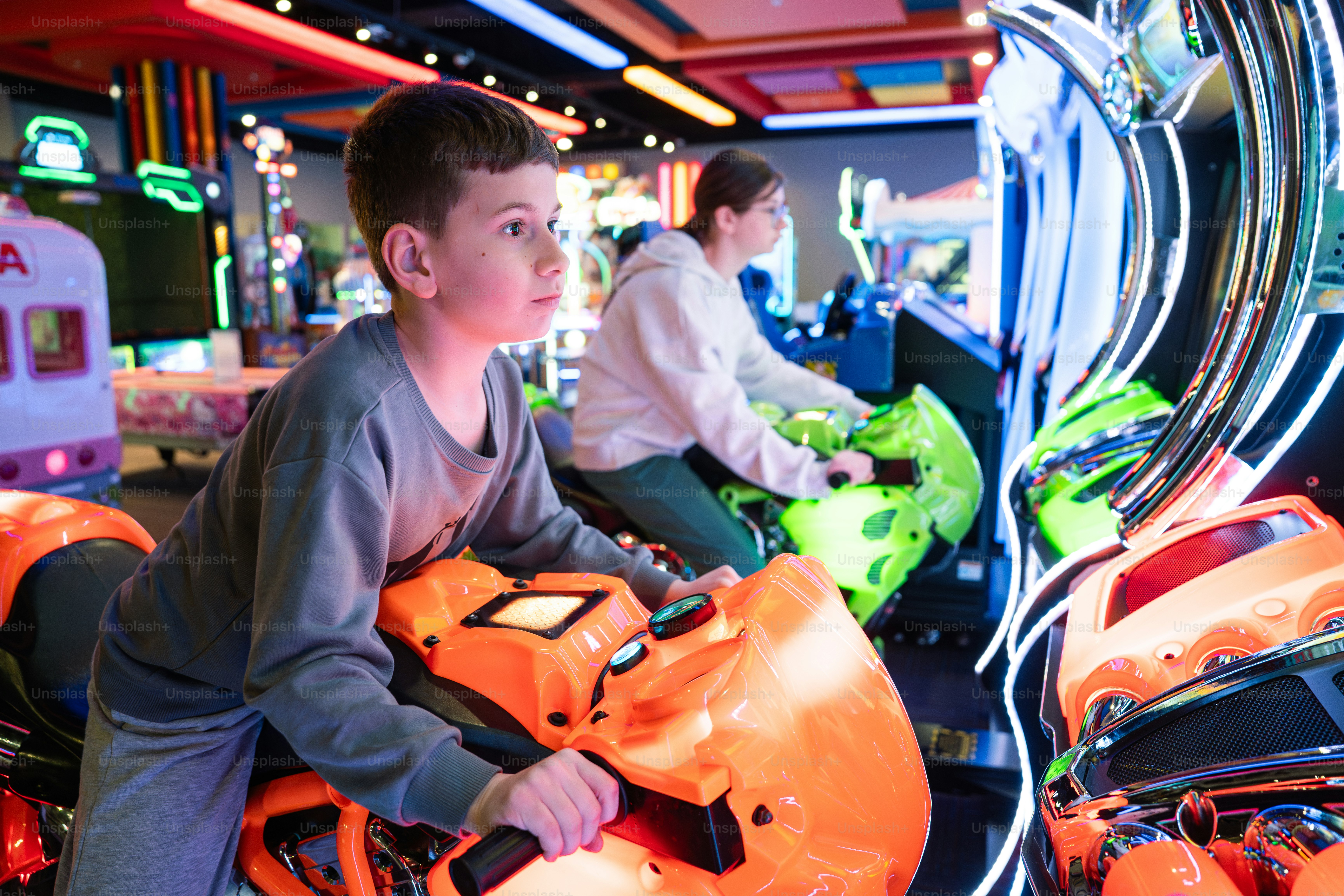 Kids are playing motorcycle racing arcade games.