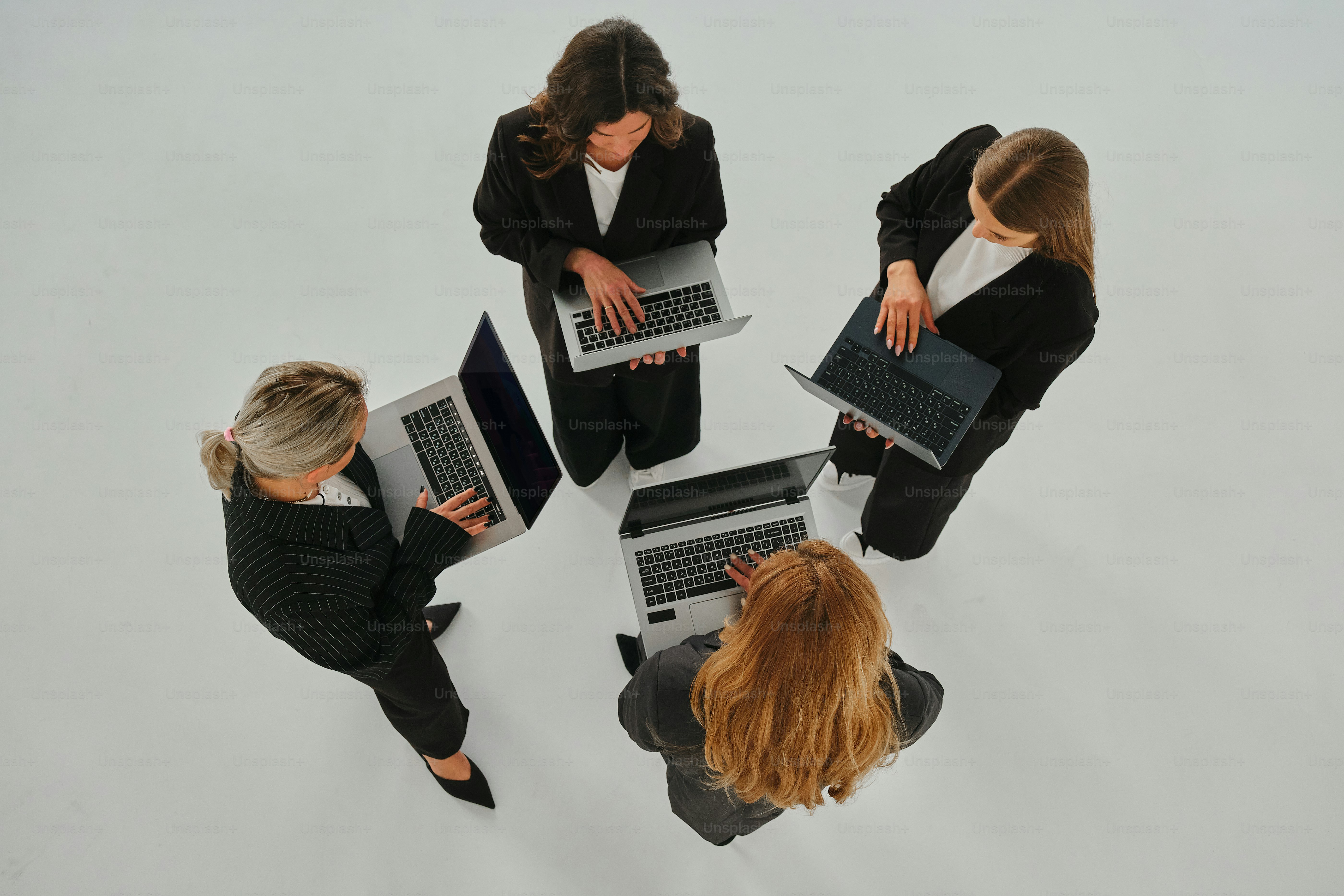Four businesswomen work on laptops in a circle.