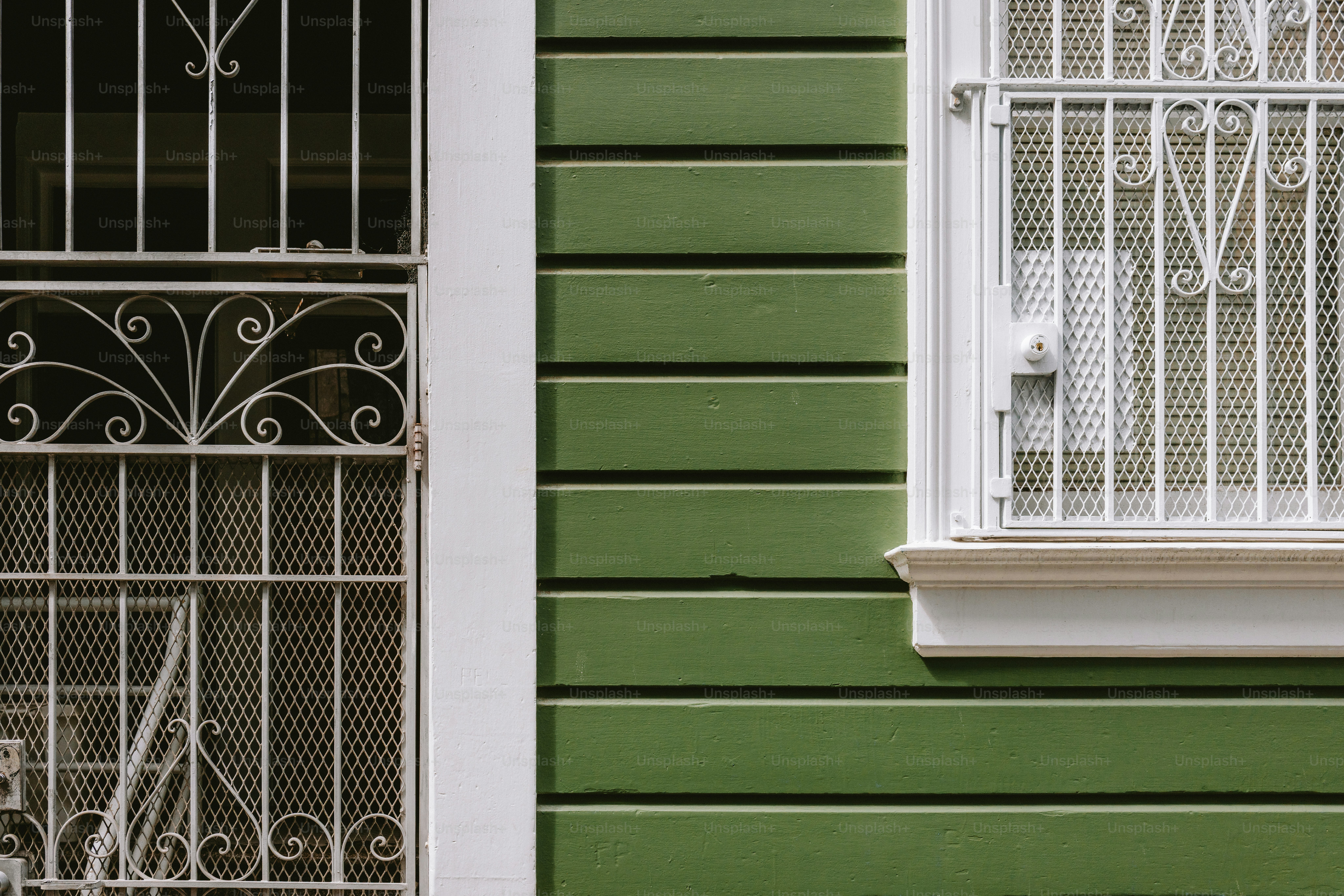 Windows with metal grates sit on a green wall.