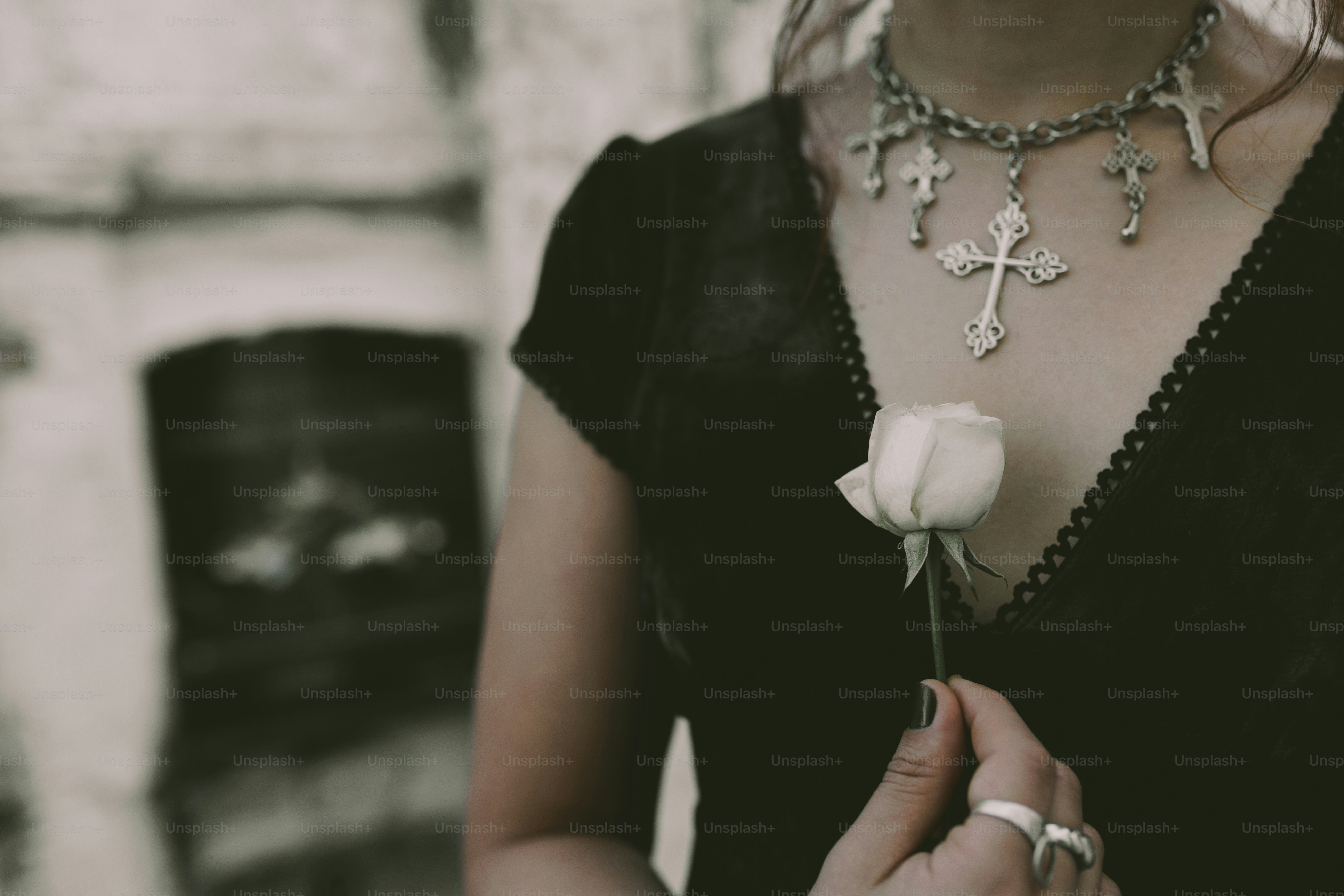 Woman in black holds a white rose and a cross necklace.