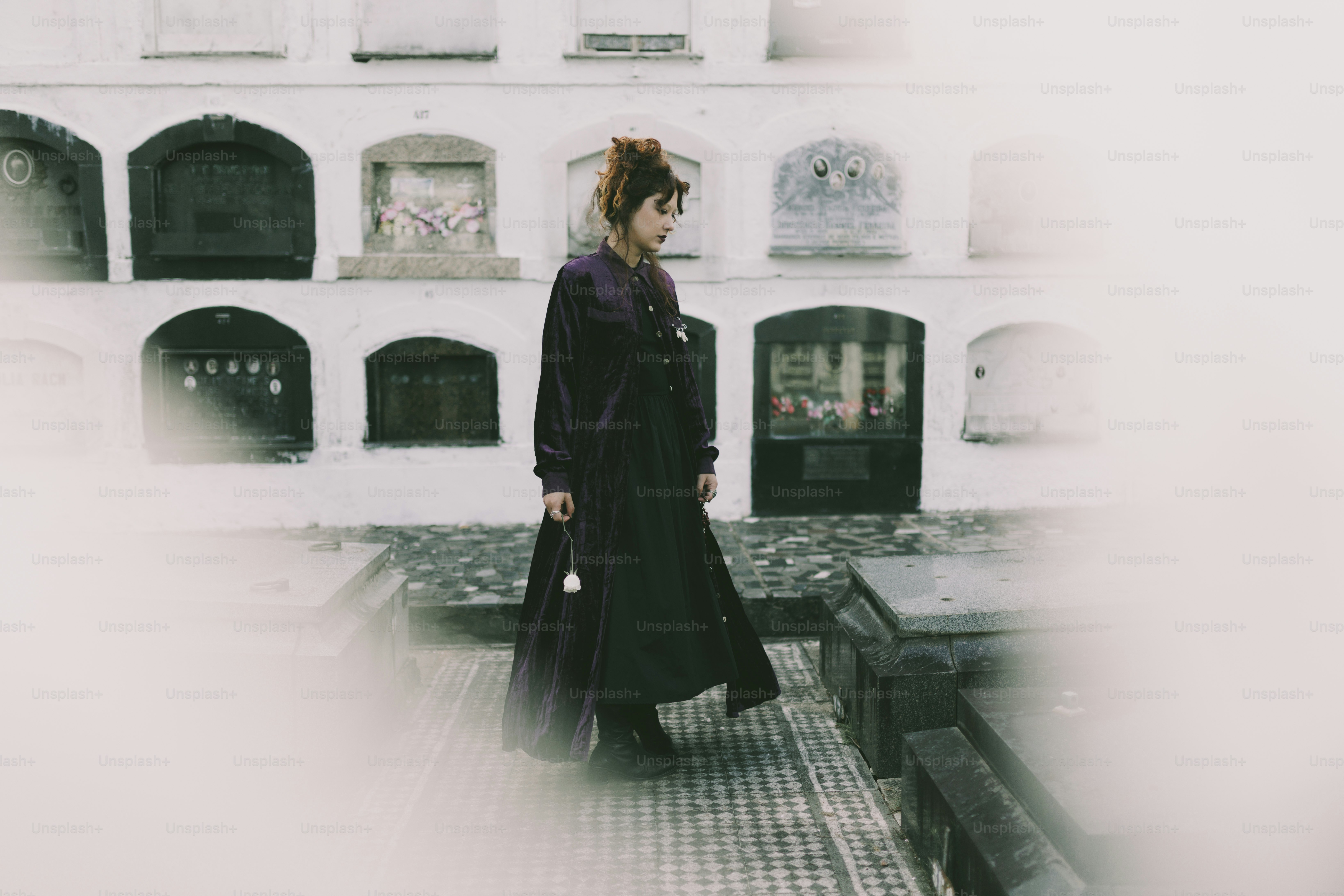 ロングコートを着た女性が墓地の墓の近くを歩きます。