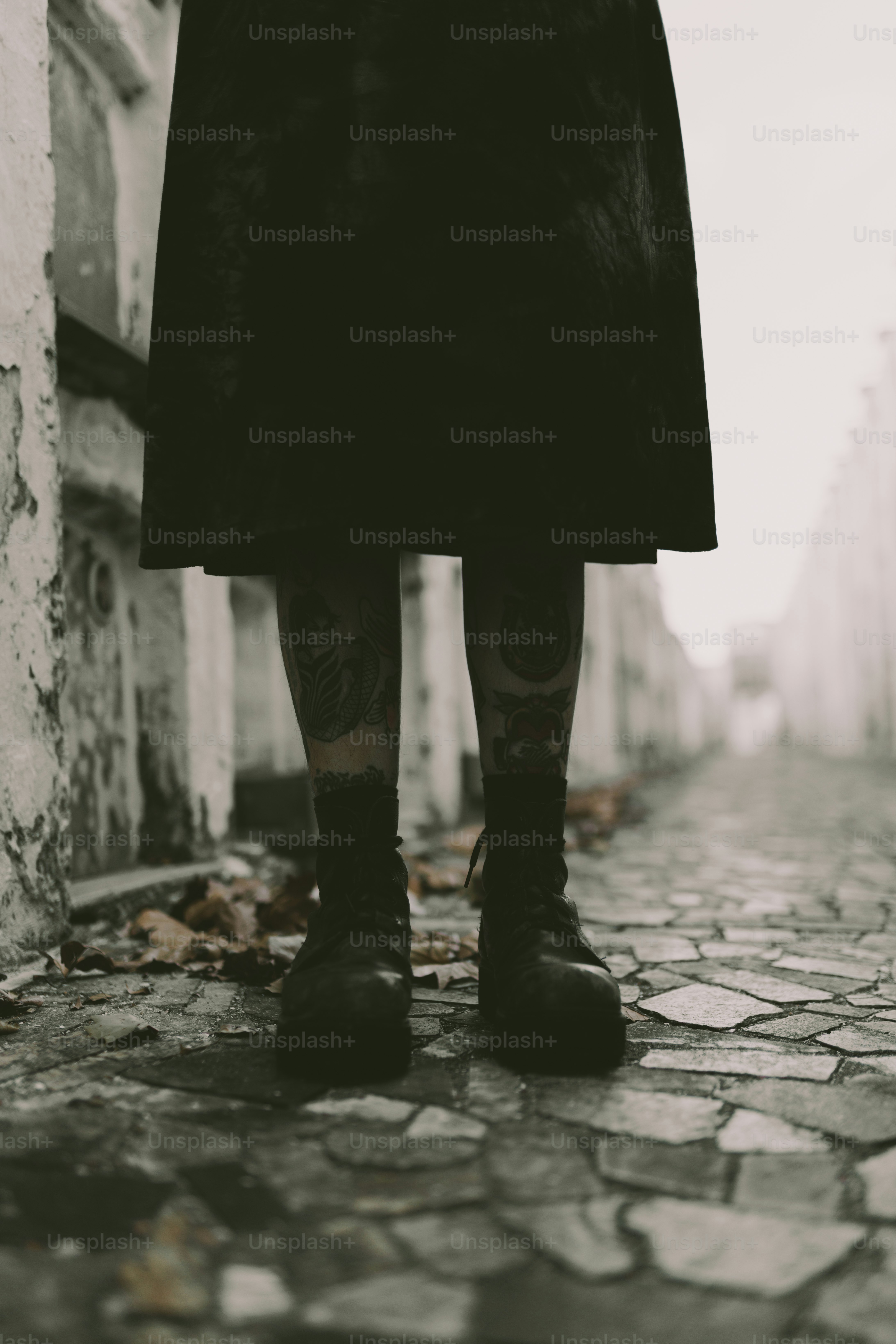 Woman with leg tattoos stands in a stone alley.