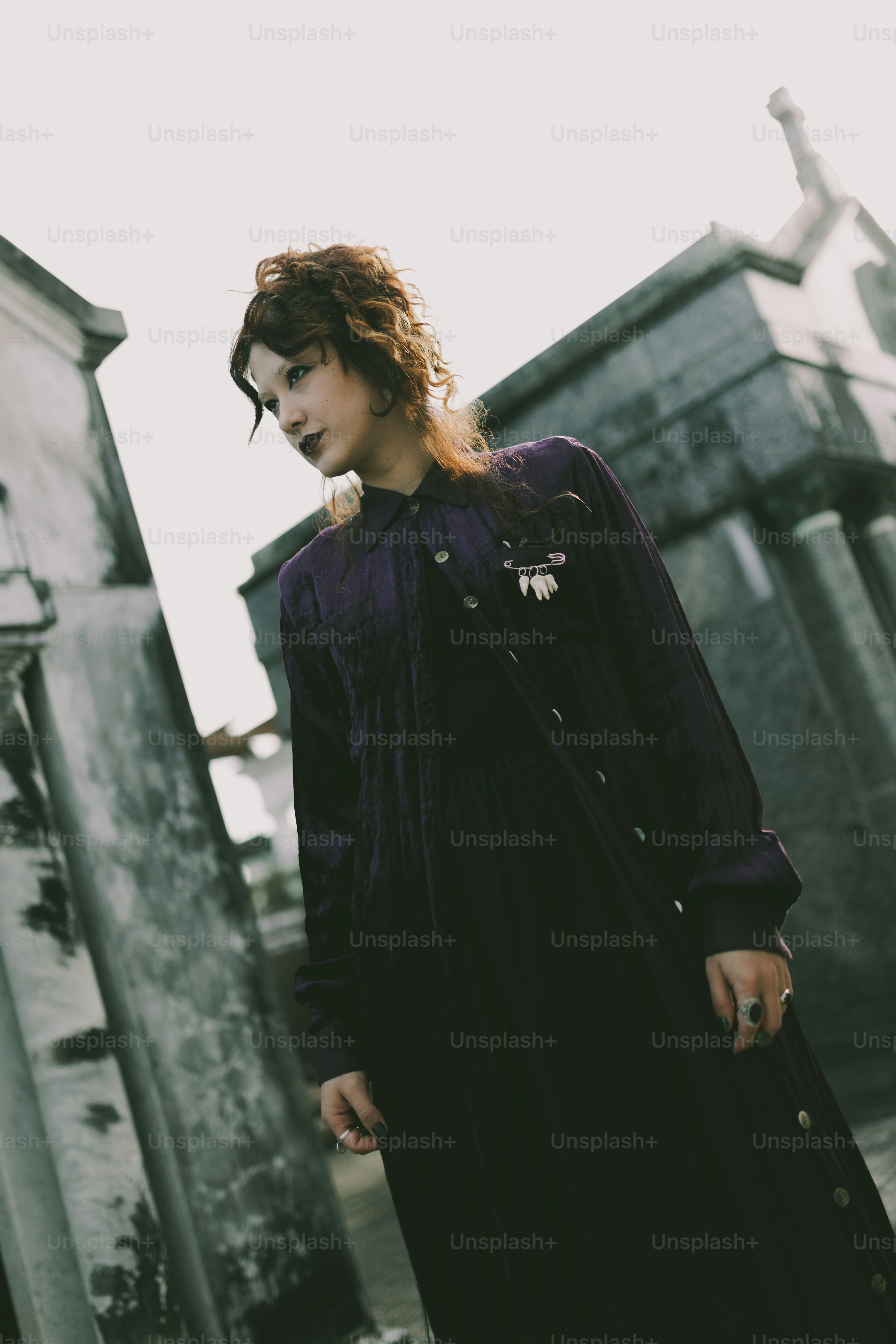 A woman in a dark outfit poses by a cemetery.