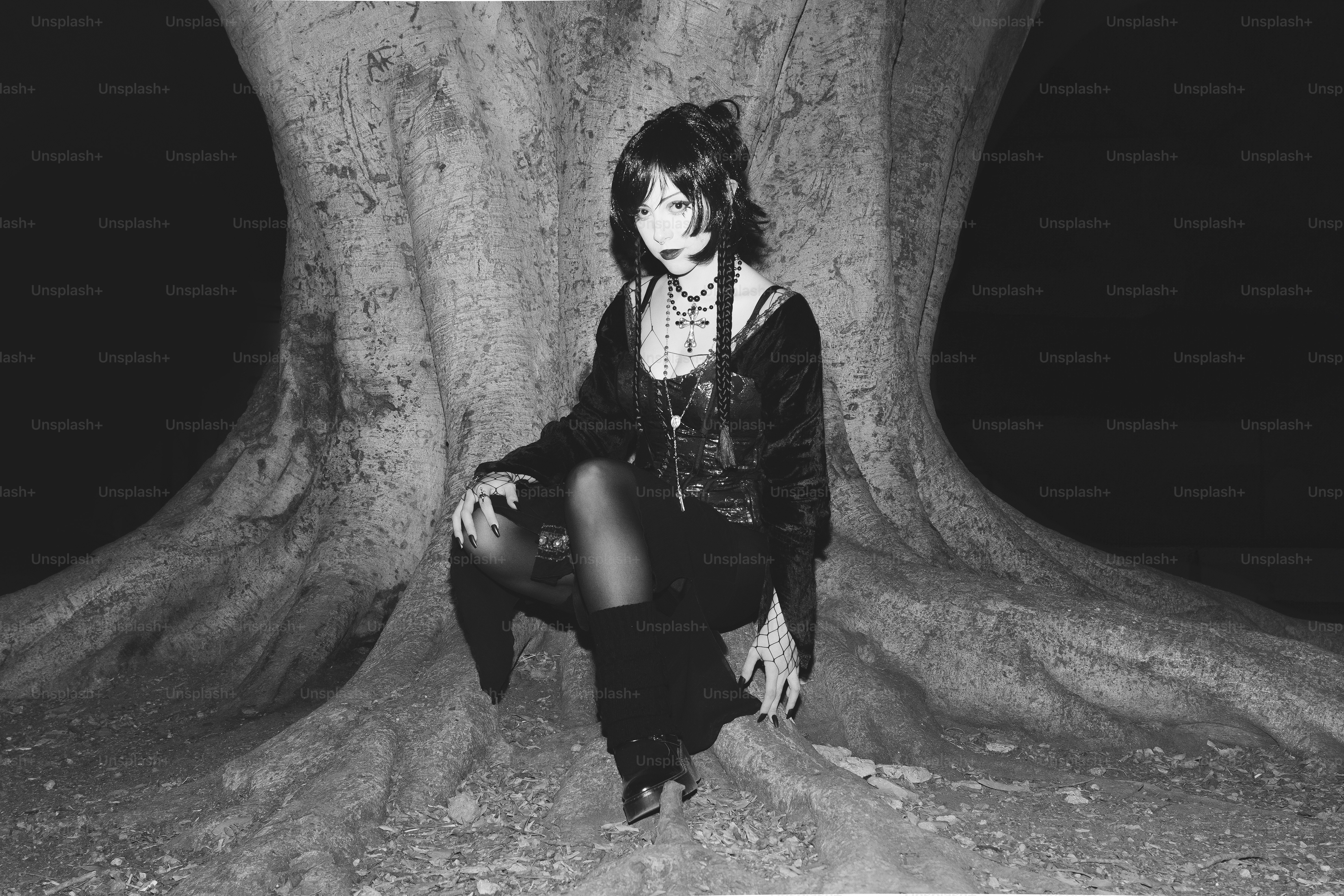 Gothic woman poses against a tree's base.