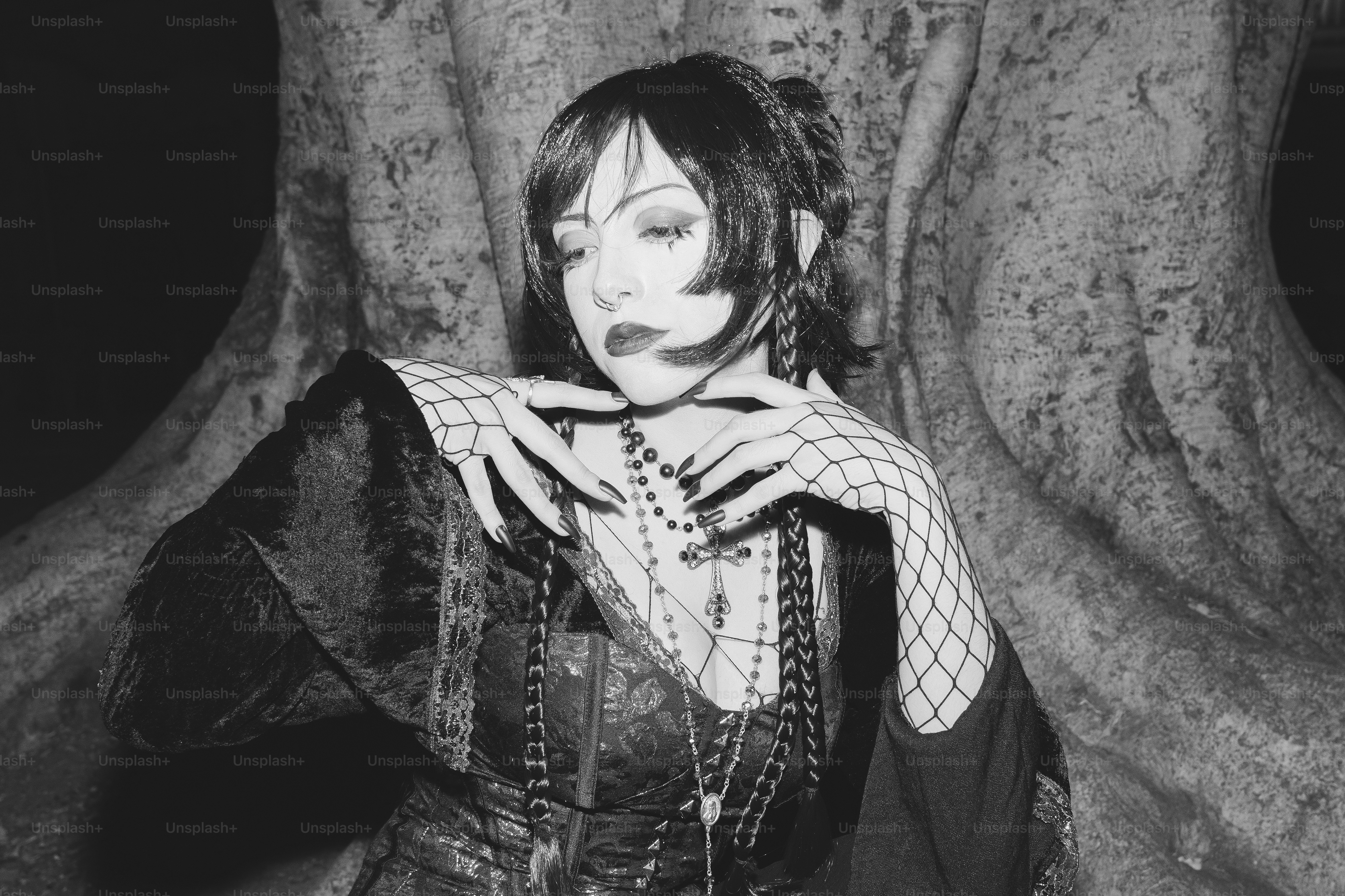 A gothic woman poses dramatically by a tree.