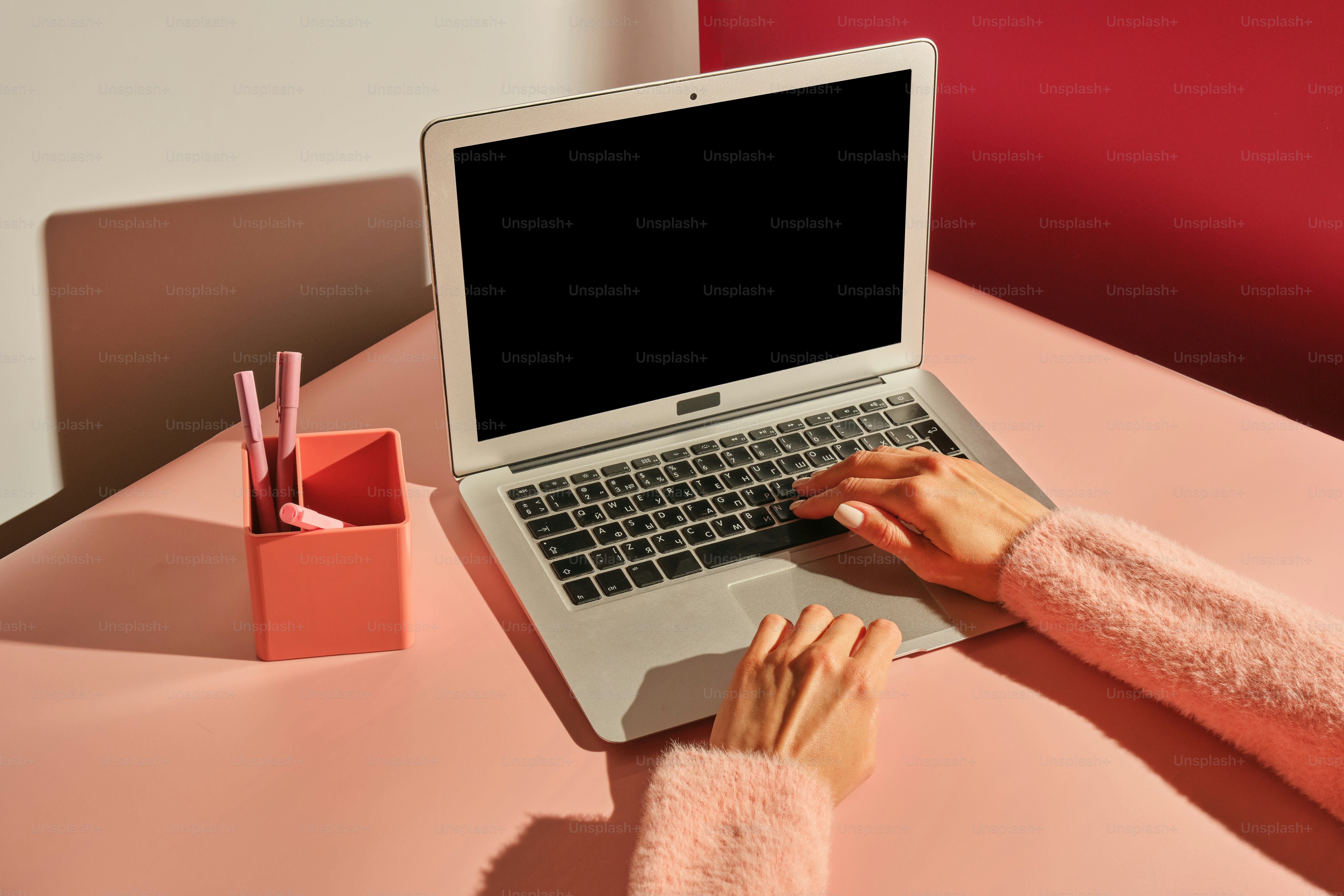 Hands type on a laptop on a pink desk.