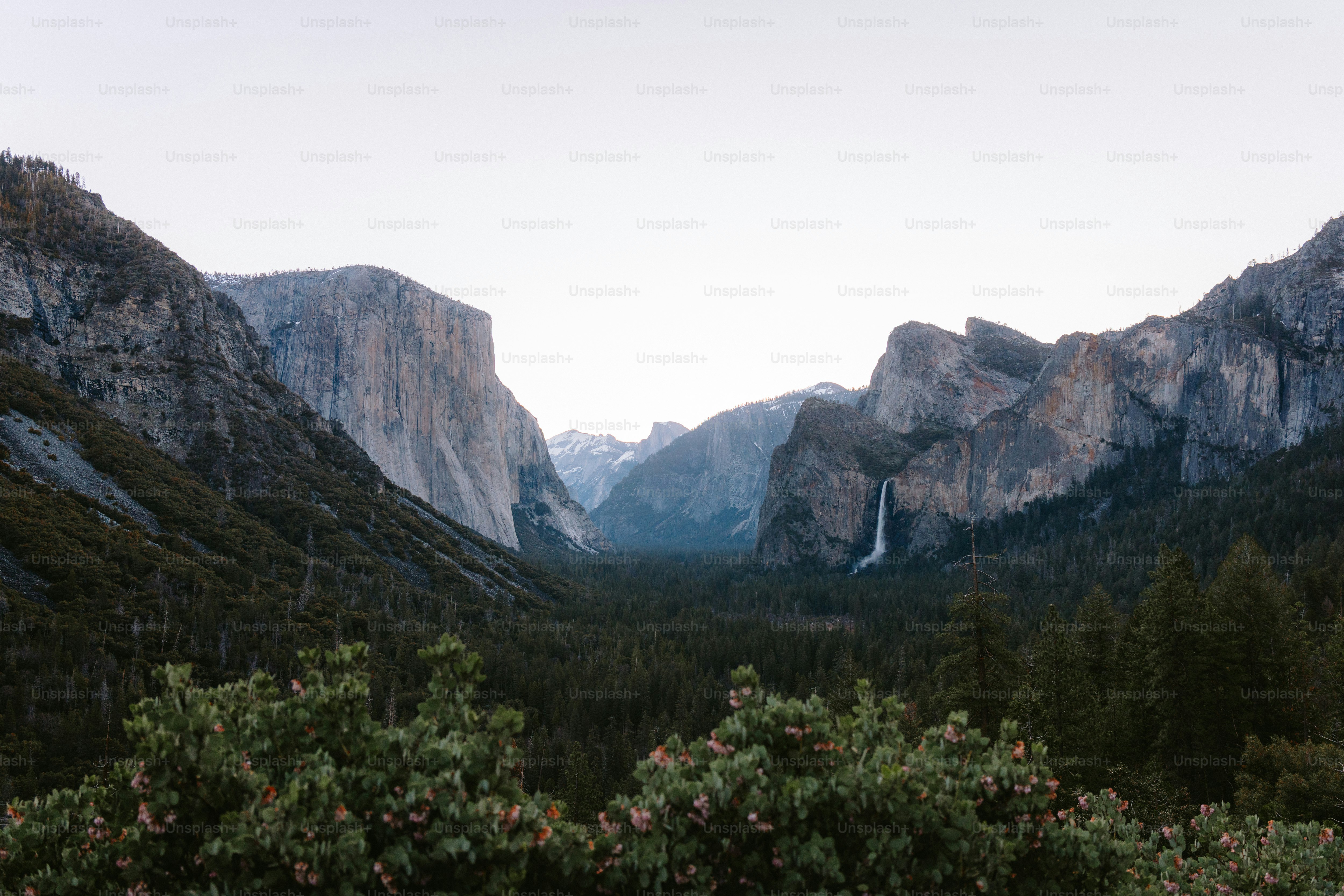Mountains frame a valley with a waterfall.