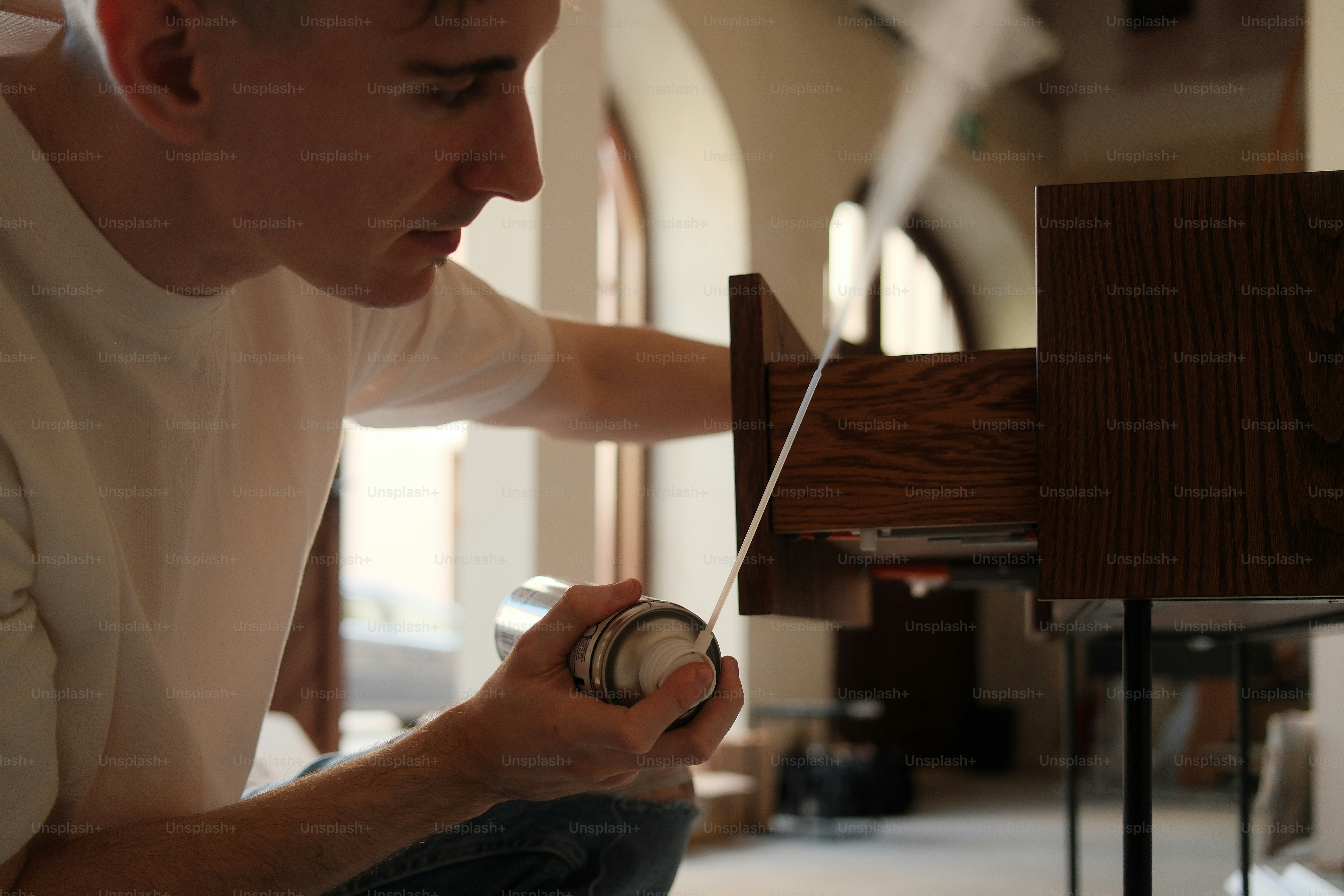 A man is spraying something on a wooden drawer.